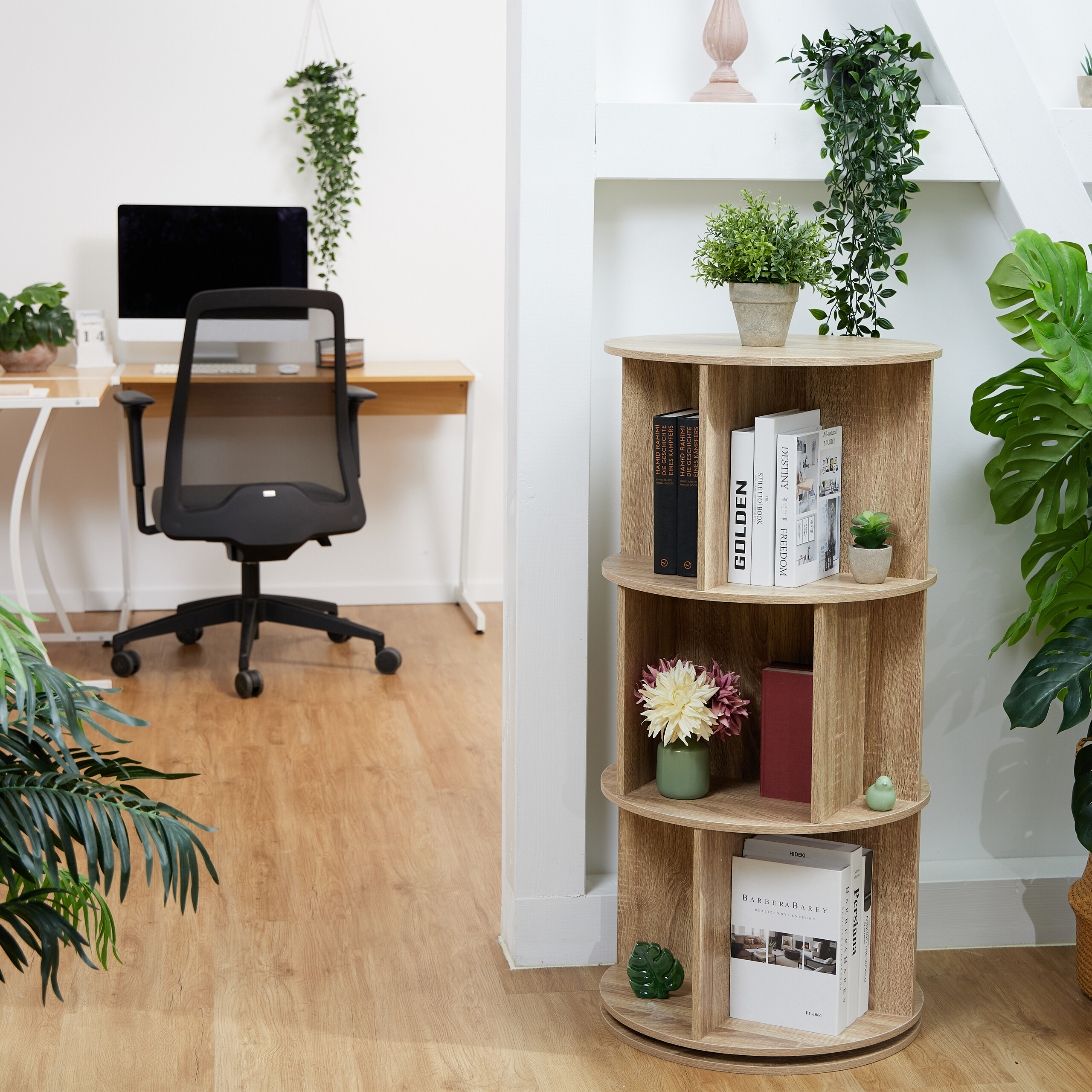Ein rundes Holzbücherregal steht in einem modernen Arbeitszimmer mit Computertisch und vielen Zimmerpflanzen.