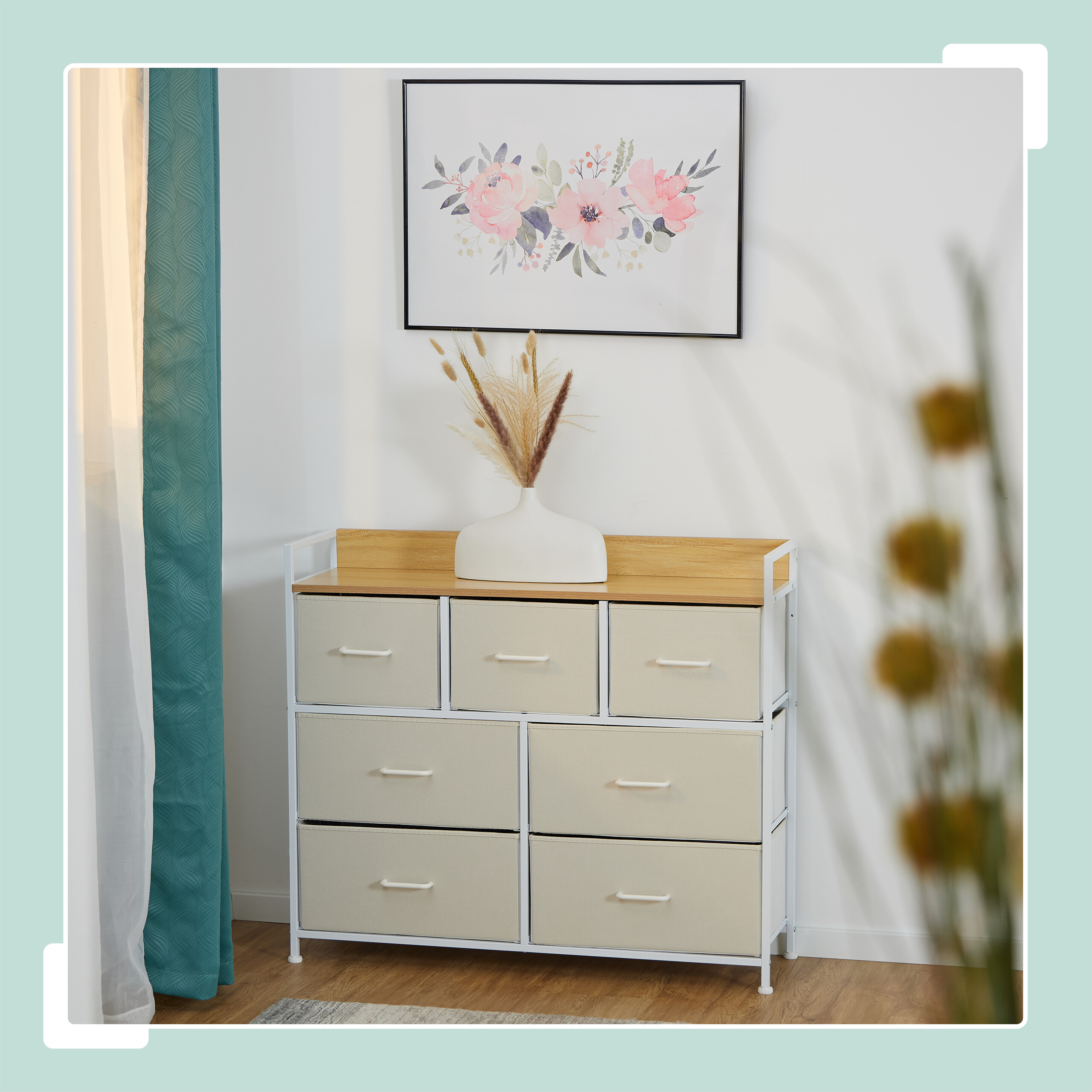 Eine weiße Kommode mit sechs beigen Stoffschubladen, einer Holzplatte, einer Vase mit Trockenblumen und einem Bild.