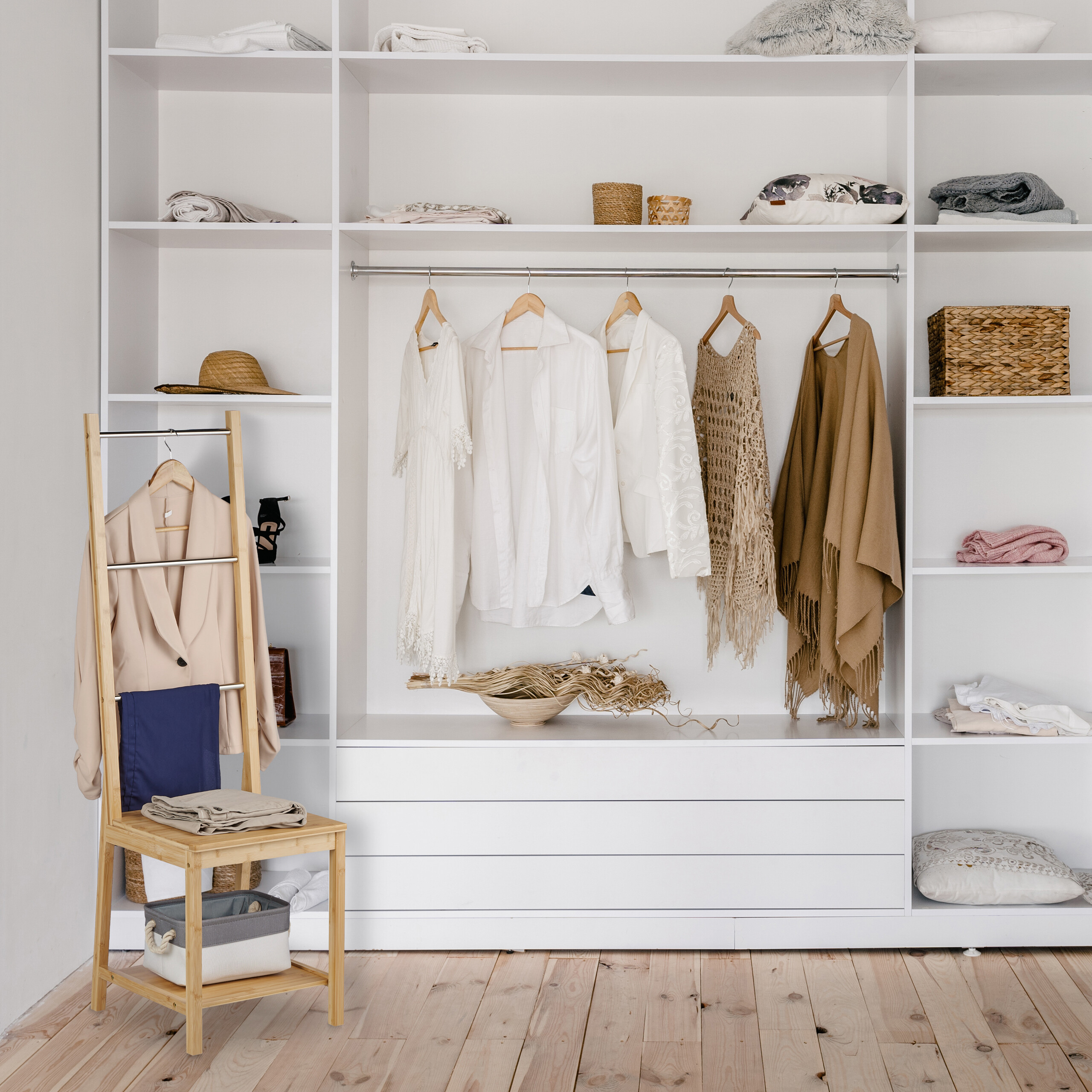Ein großer weißer begehbarer Kleiderschrank mit geordneter Kleidung, Accessoires und einem Holzleiterstuhl.