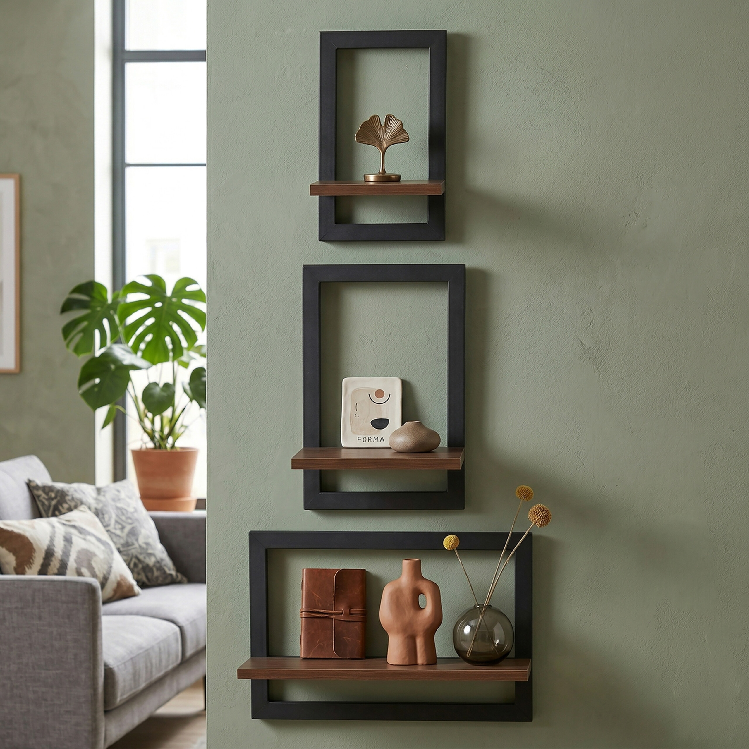 Drei schwarze Rahmenregale mit Dekoration hängen an einer grünen Wand in einem Wohnzimmer.