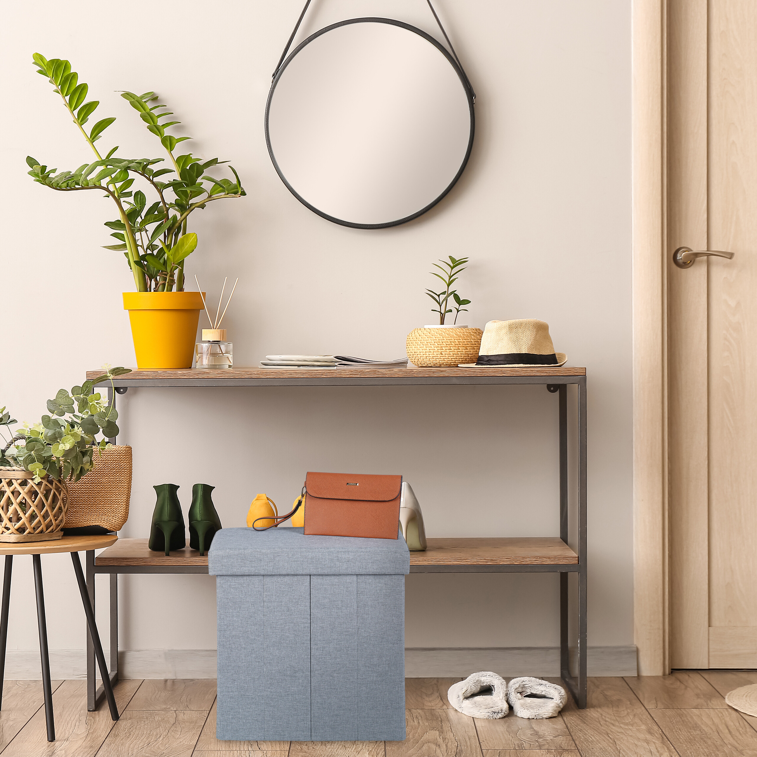 Ein Flur mit Konsole, Pflanzen, rundem Spiegel und blauem Hocker mit brauner Handtasche.
