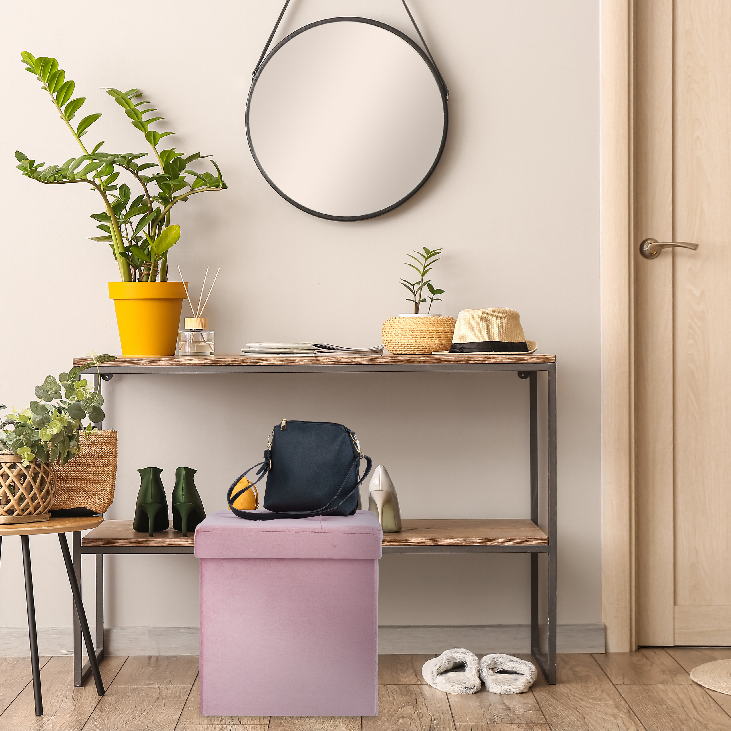 Ein Flur mit Konsole, rundem Spiegel, Pflanzen, Hut und einem rosa Hocker mit blauer Tasche.