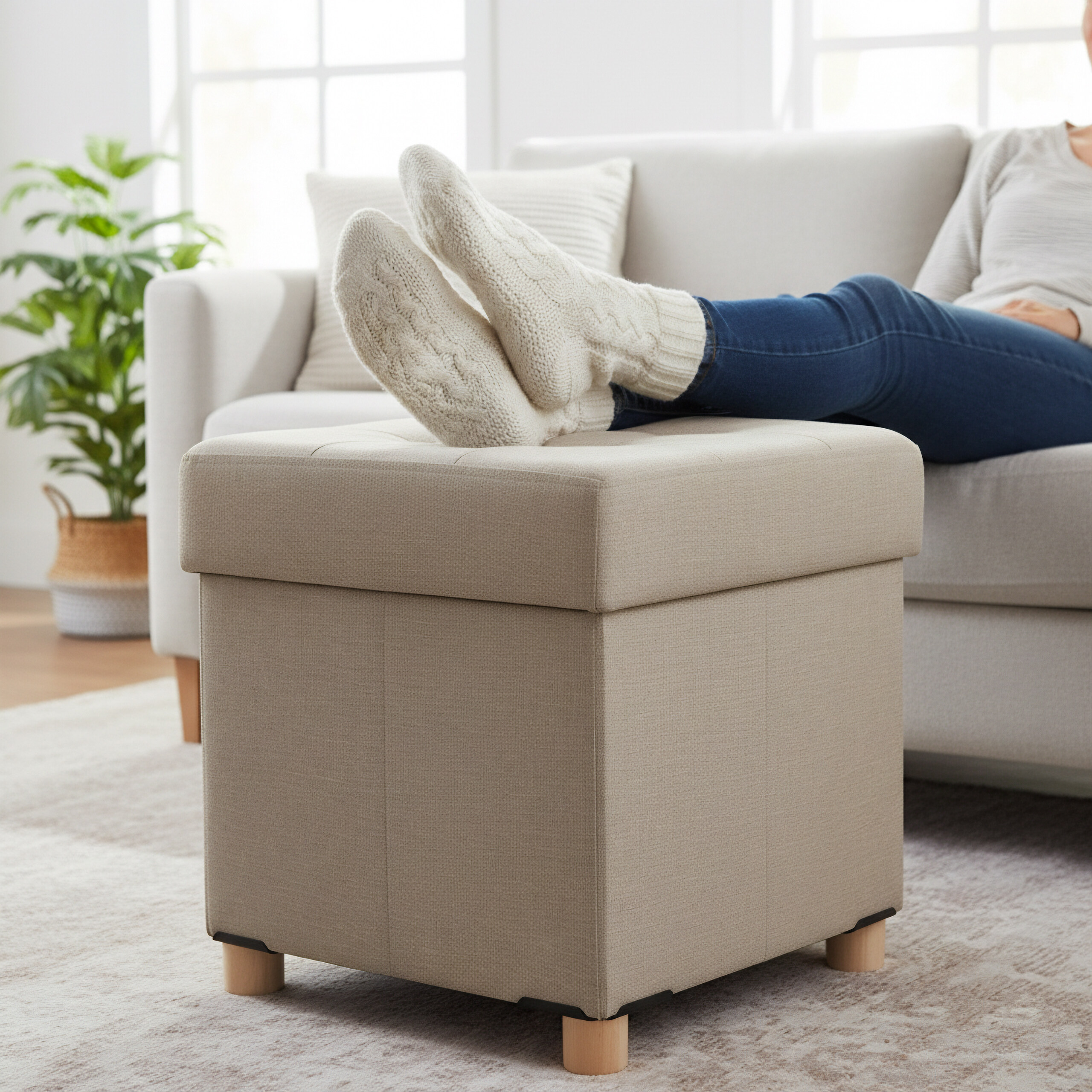 Eine Person sitzt auf einem Sofa und legt die Füße in weißen Wollsocken auf einen beigen Hocker.
