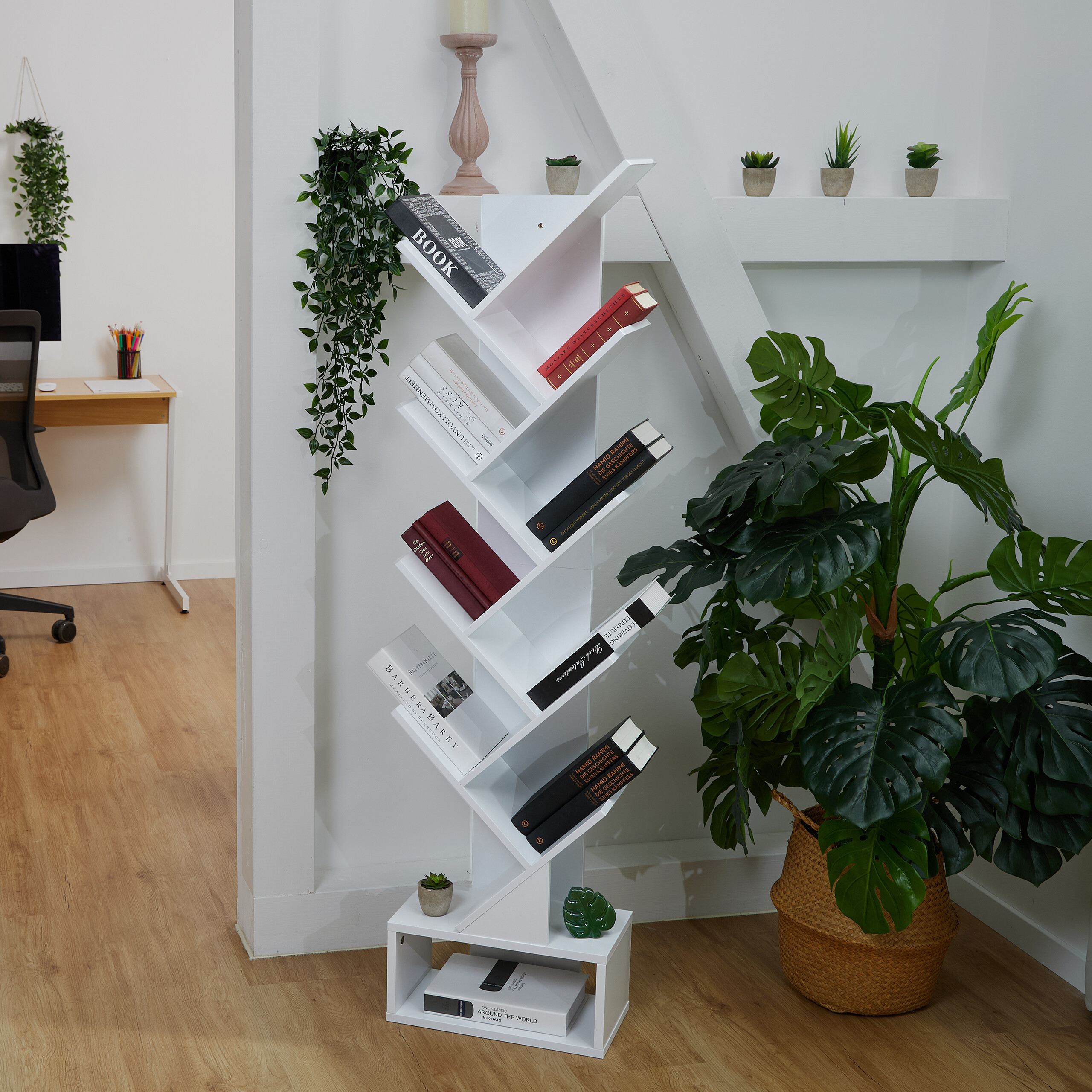 Ein weißes, baumförmiges Bücherregal mit Büchern steht in einem modernen Raum mit Pflanzen und hellem Holzboden.