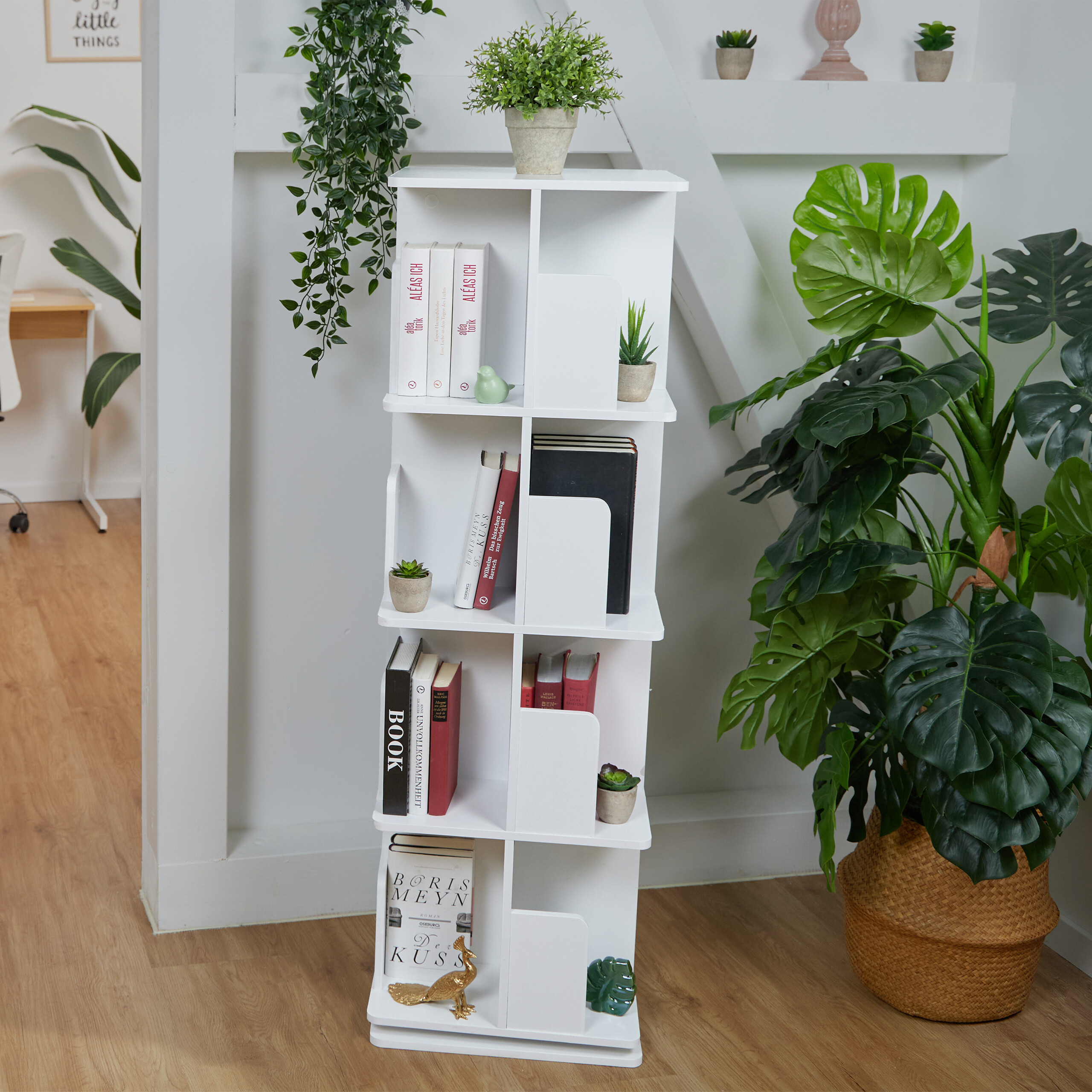 Ein weißes Bücherregal mit verschiedenen Büchern, Dekorationsgegenständen und Pflanzen in einem hellen Raum.