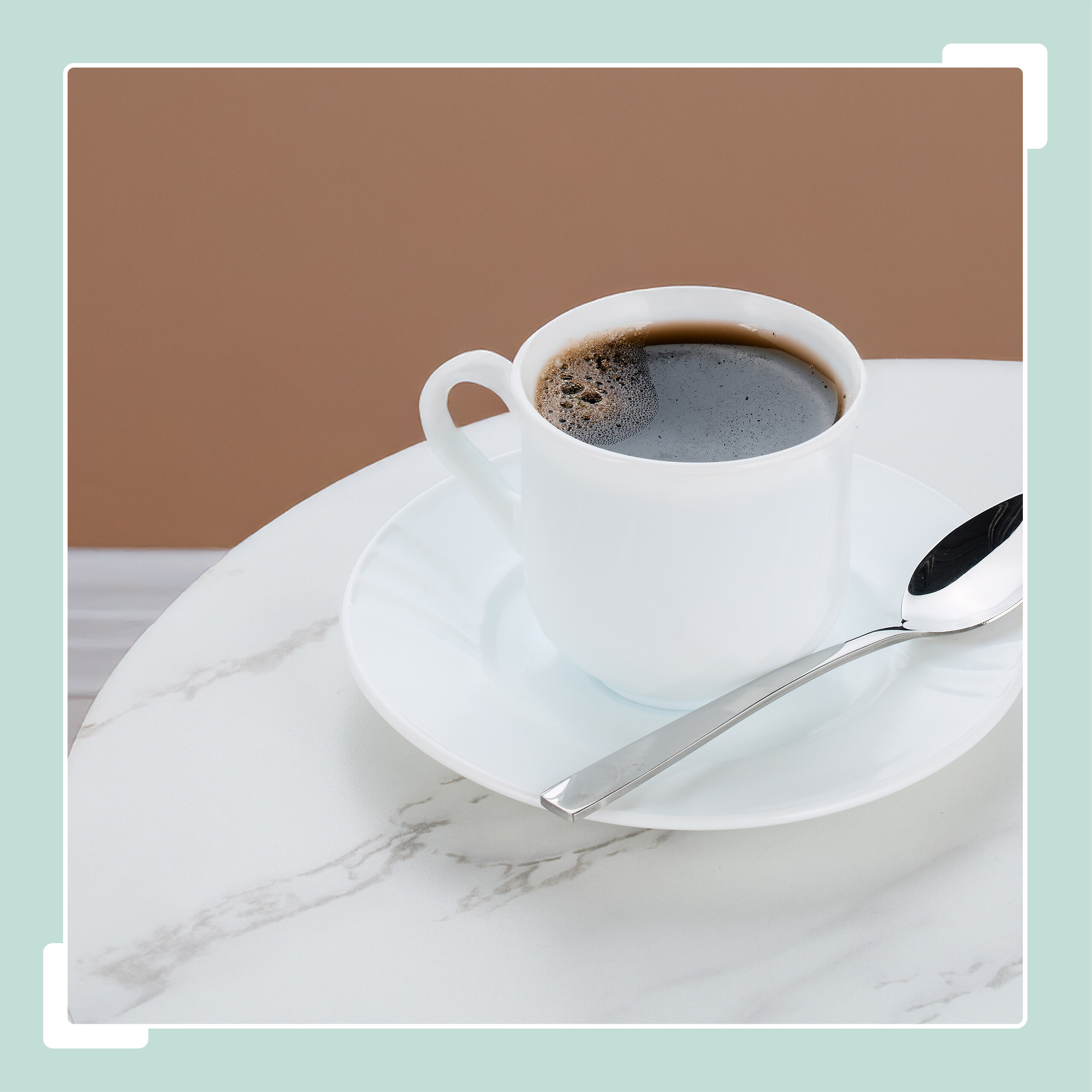 Eine weiße Kaffeetasse mit Untertasse und Löffel auf einem Marmortisch.