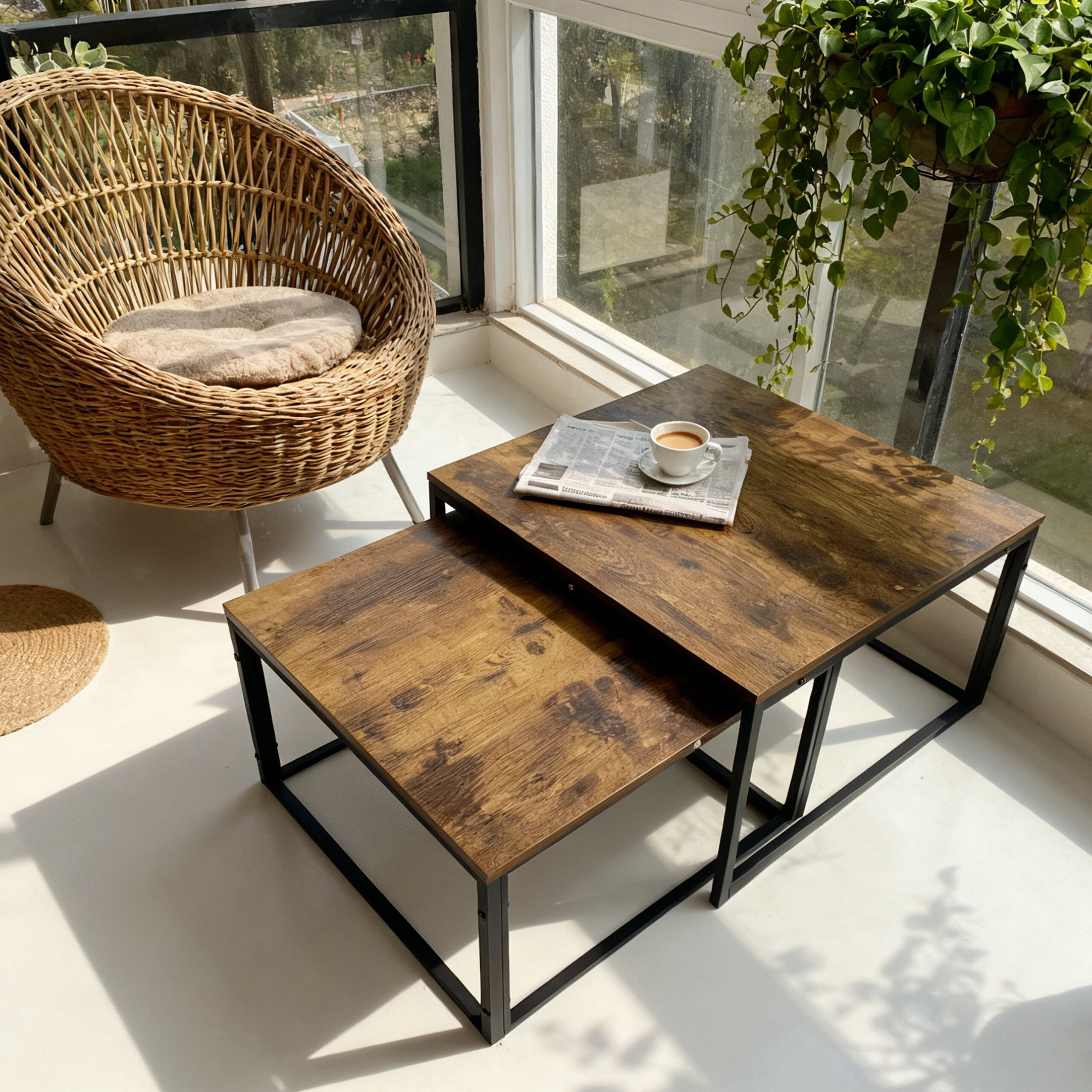 Ein Rattansessel und zwei Holztische mit Zeitung und Tasse Kaffe am sonnigen Fenster.