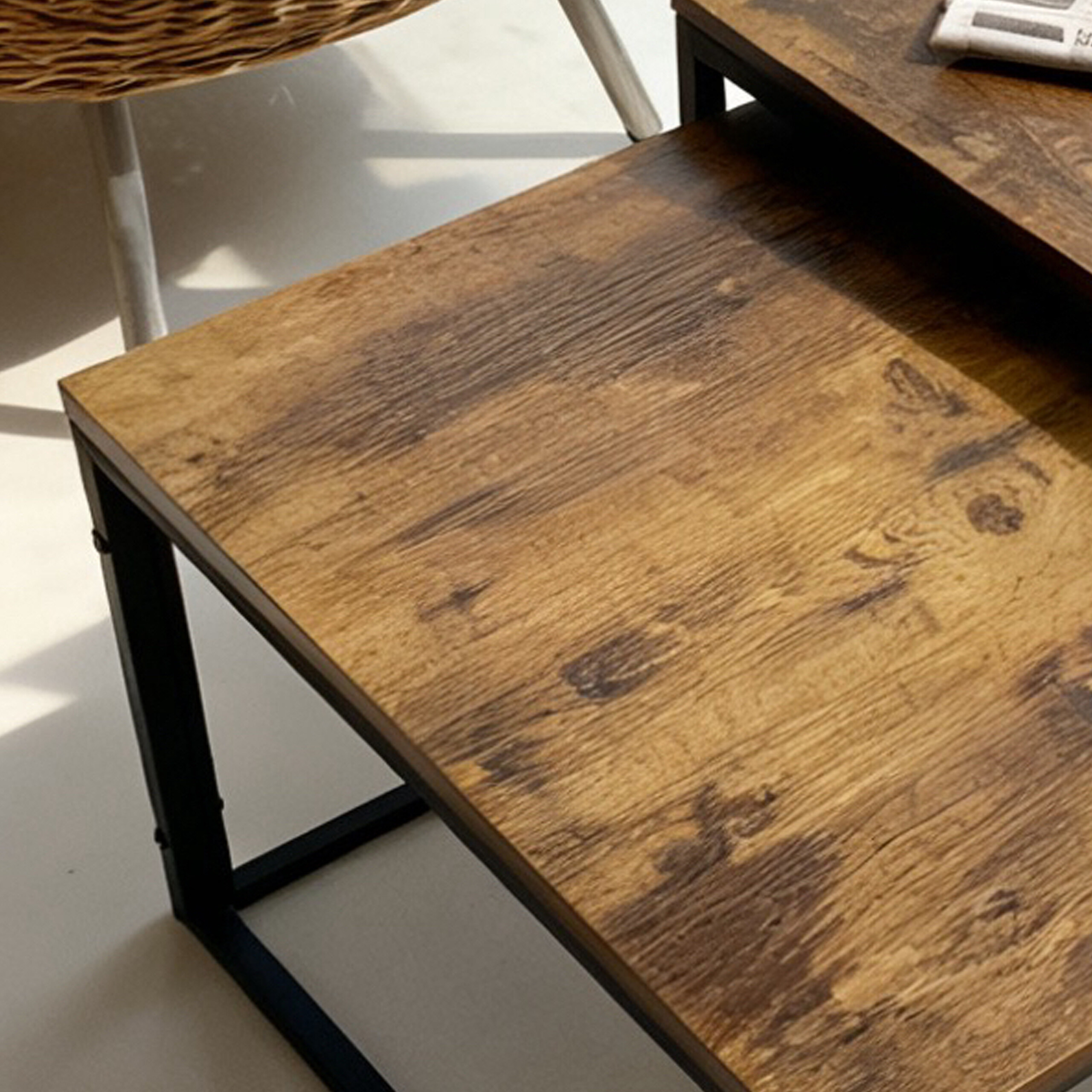 Zwei Holztische mit schwarzem Metallgestell stehen auf hellem Boden neben einem Rattansessel.