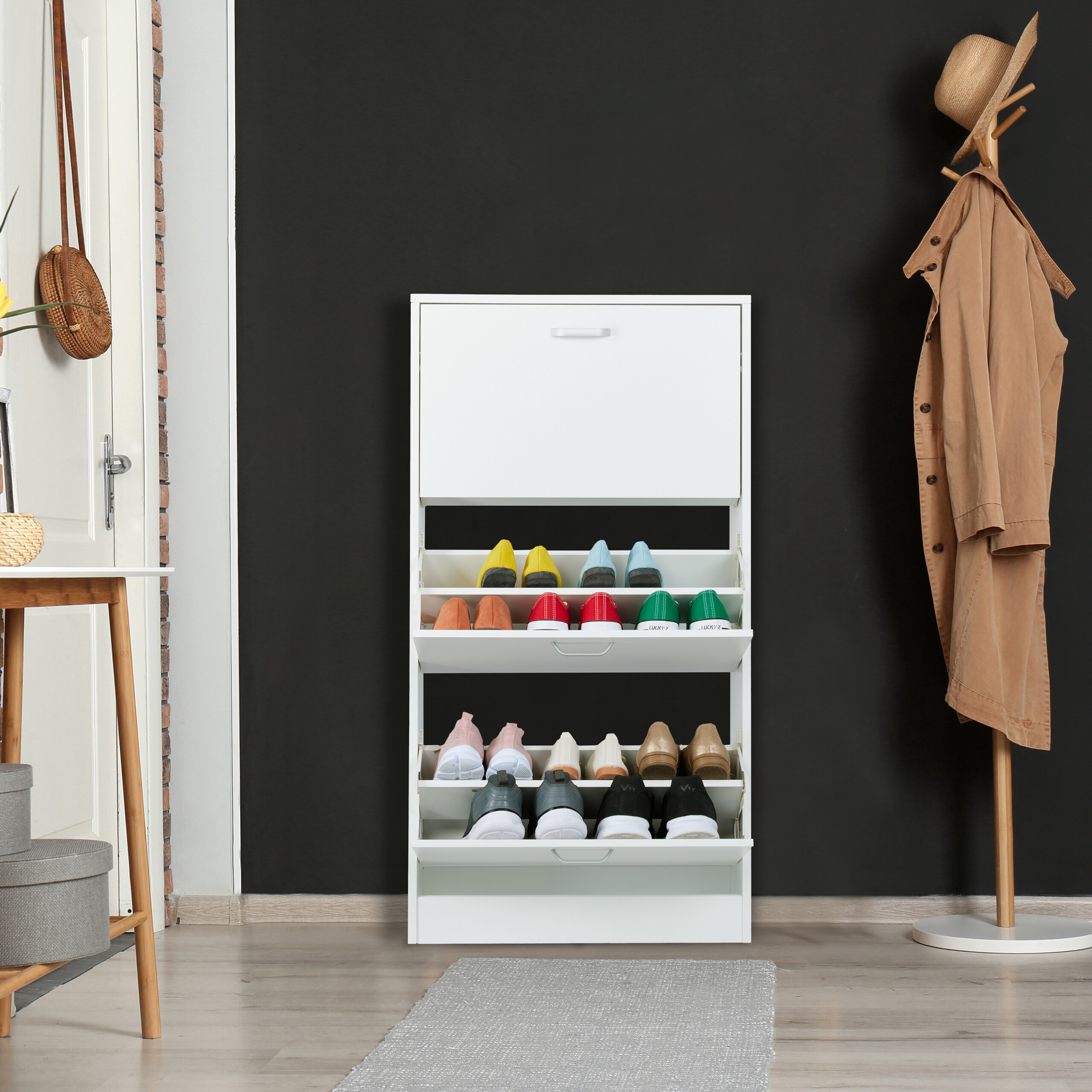Ein weißer Schuhschrank mit bunten Schuhen steht an einer schwarzen Wand, neben einer Garderobe und einer weißen Tür.