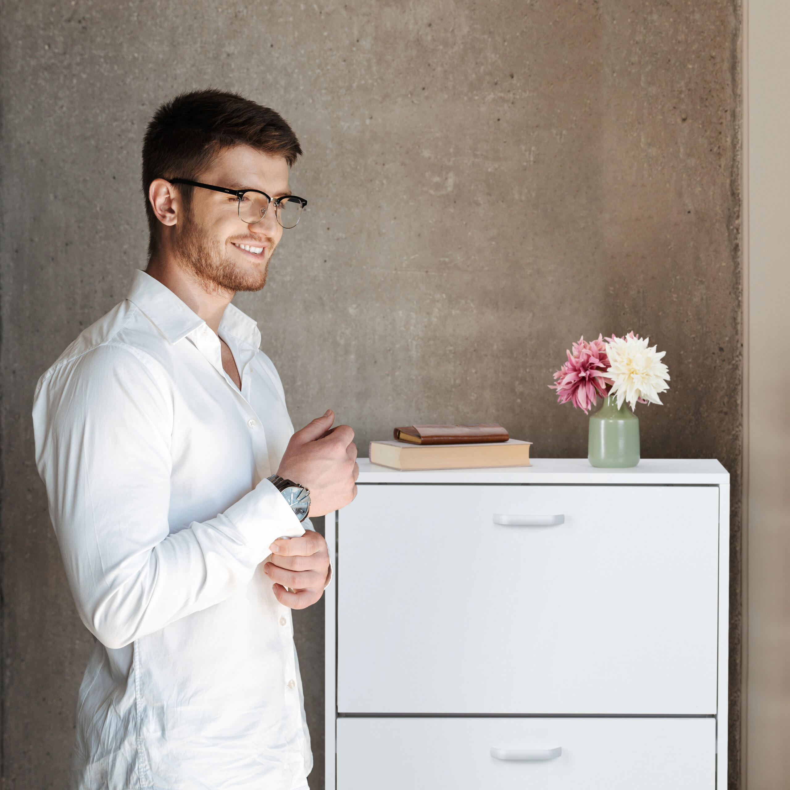 Mann mit Brille und weißem Hemd lächelt vor einer Betonwand.