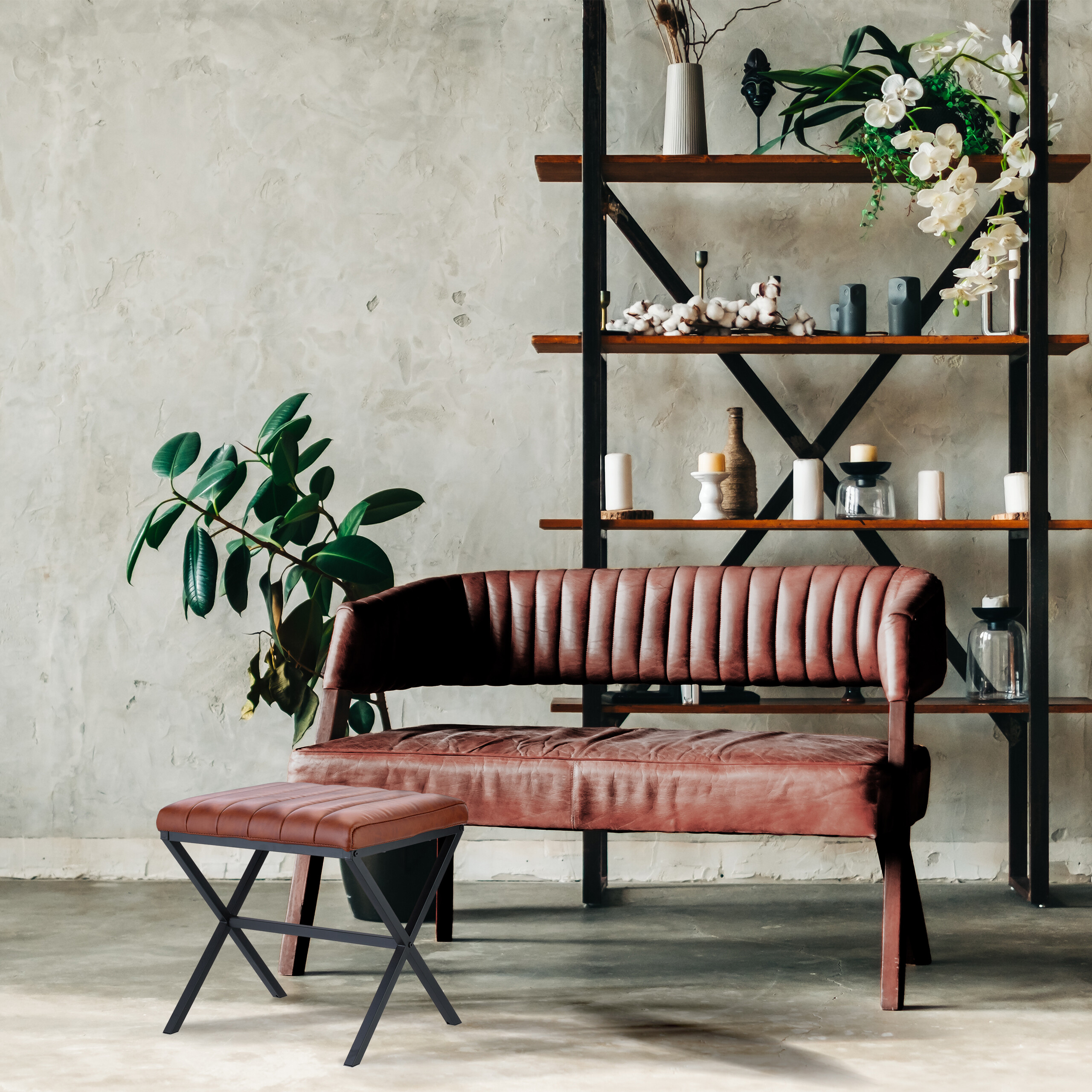 Ein braunes Ledersofa und ein passender Hocker vor einem Metallregal an einer grauen Wand.