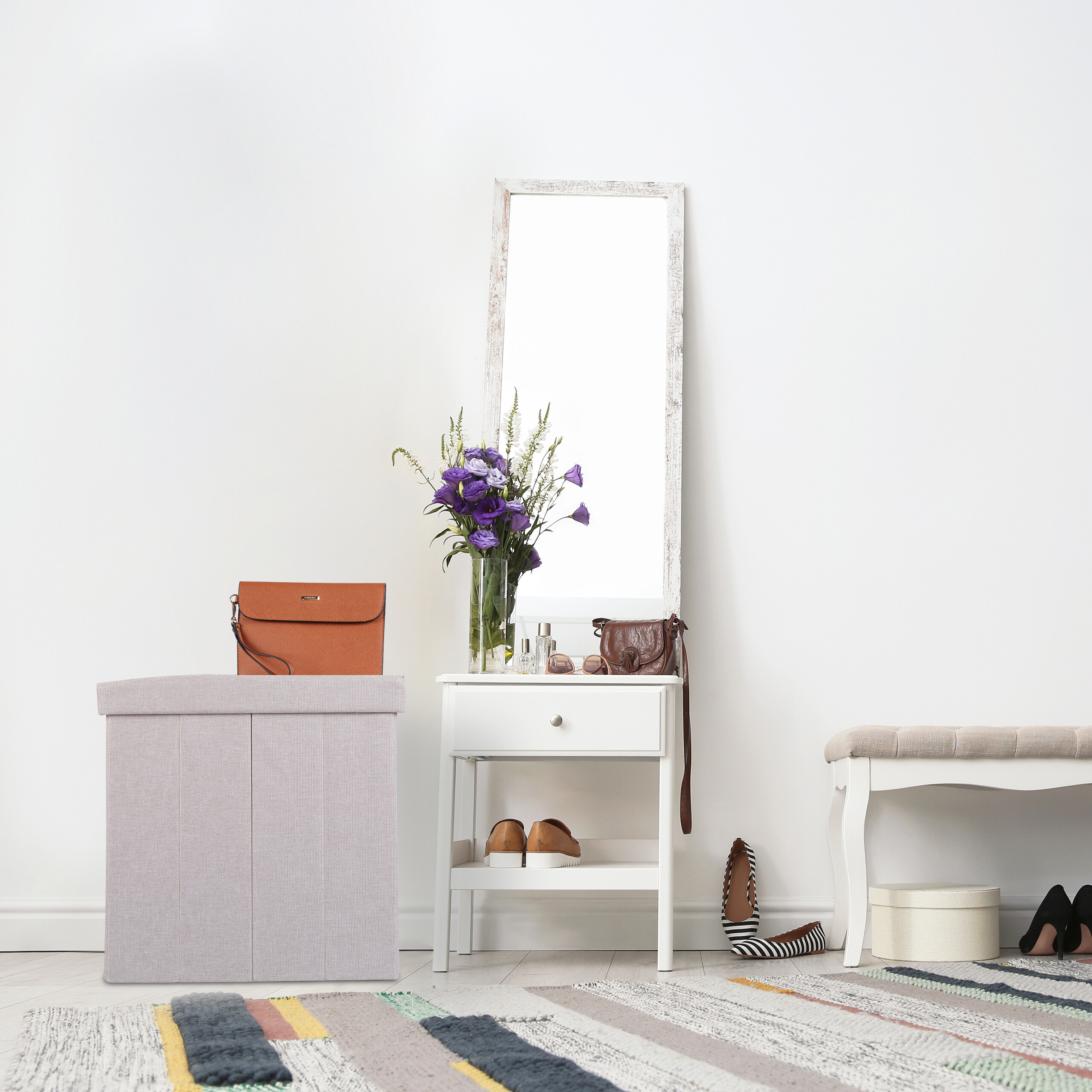 Ein weißer Tisch mit Spiegel, Blumenstrauß, Handtaschen, Schuhen und einer Sitzbank in einem hellen Raum.