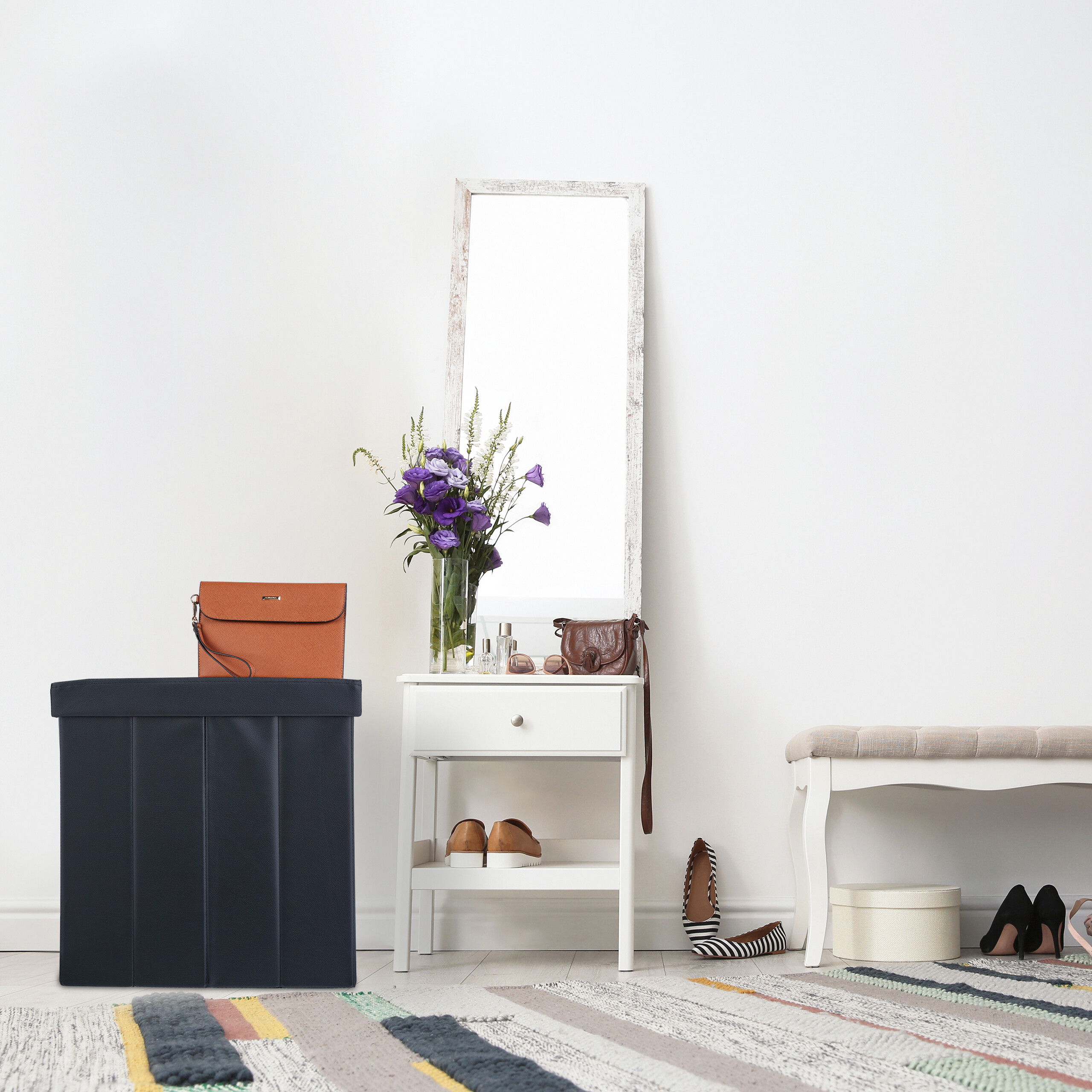 Ein weißer Flur mit einem Spiegel, einem kleinen Tisch mit lila Blumen, einer dunklen Box, einer Bank und Schuhen.