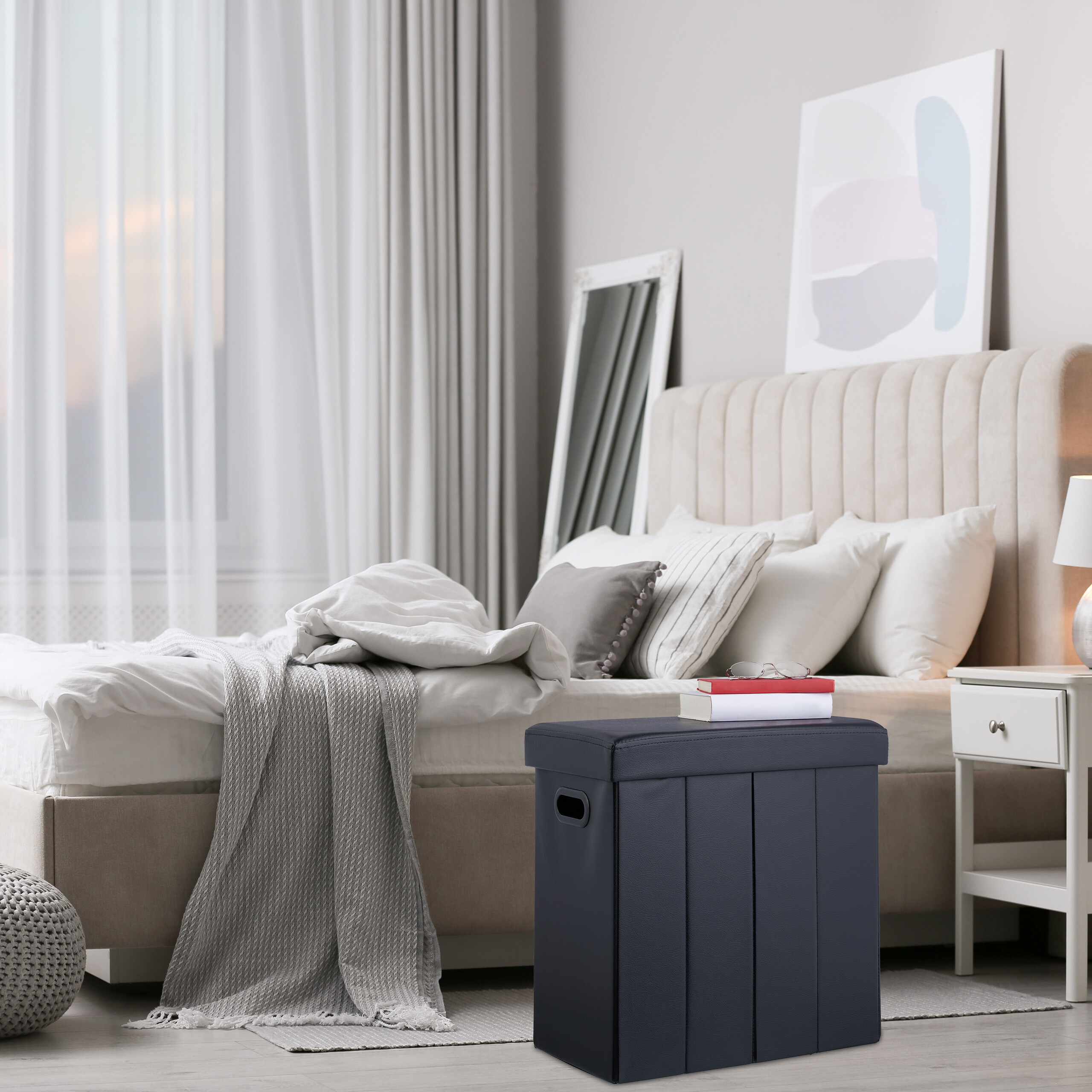Ein grauer Stauraumhocker steht vor einem beige gepol-sterten Bett in einem hellen Schlafzimmer.