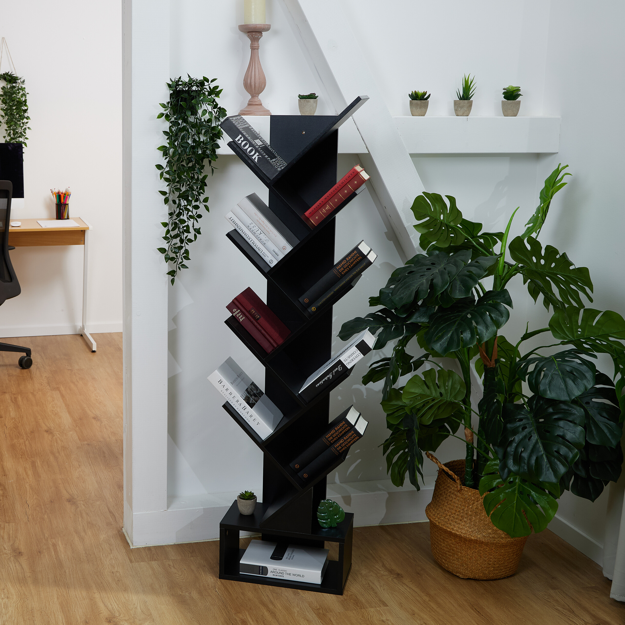 Ein schwarzes holzregal mit büchern steht in einem raum neben einer großen pflanze.
