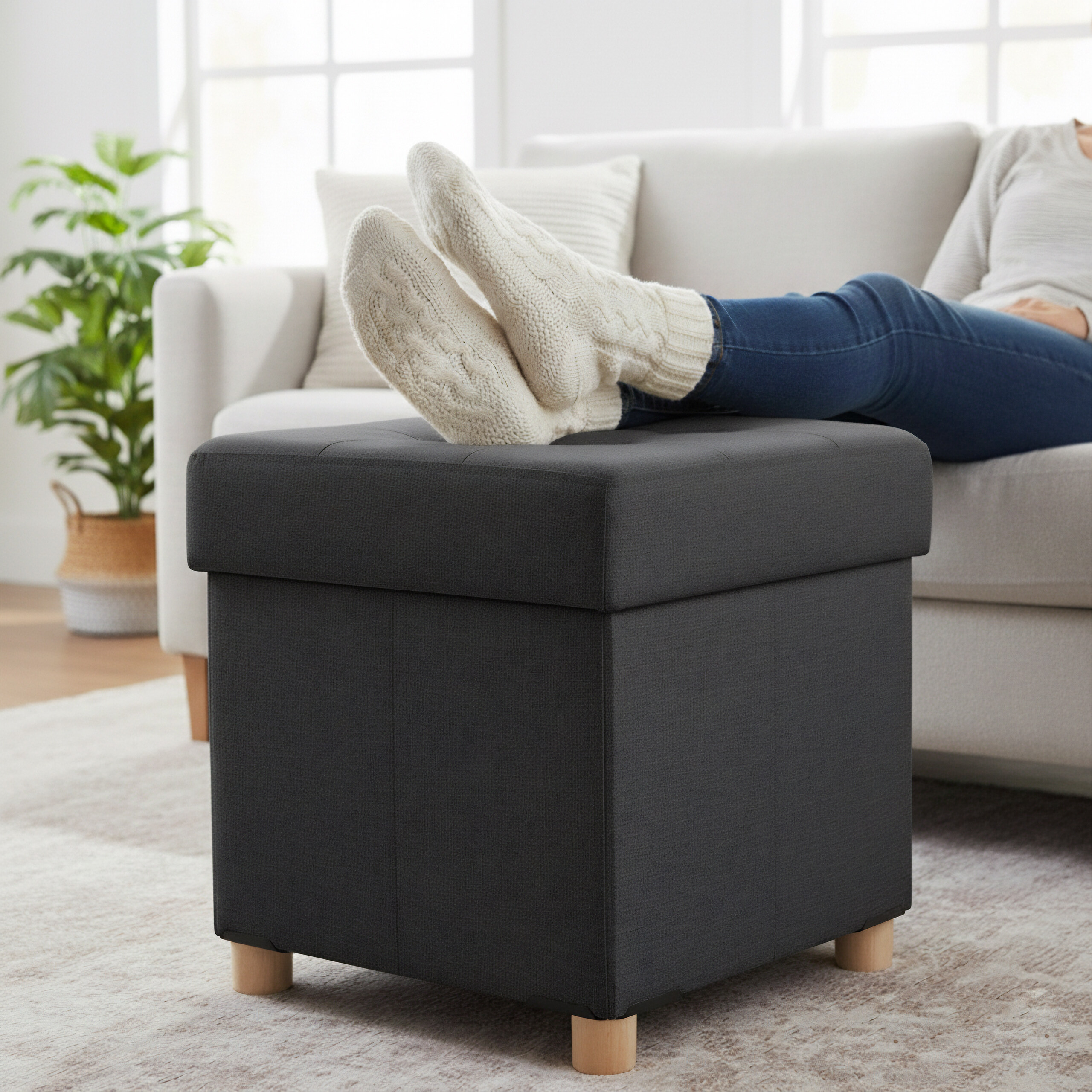 Eine Person sitzt mit dicken Wollsocken auf dem Sofa und legt die Füße auf einen dunklen Hocker.