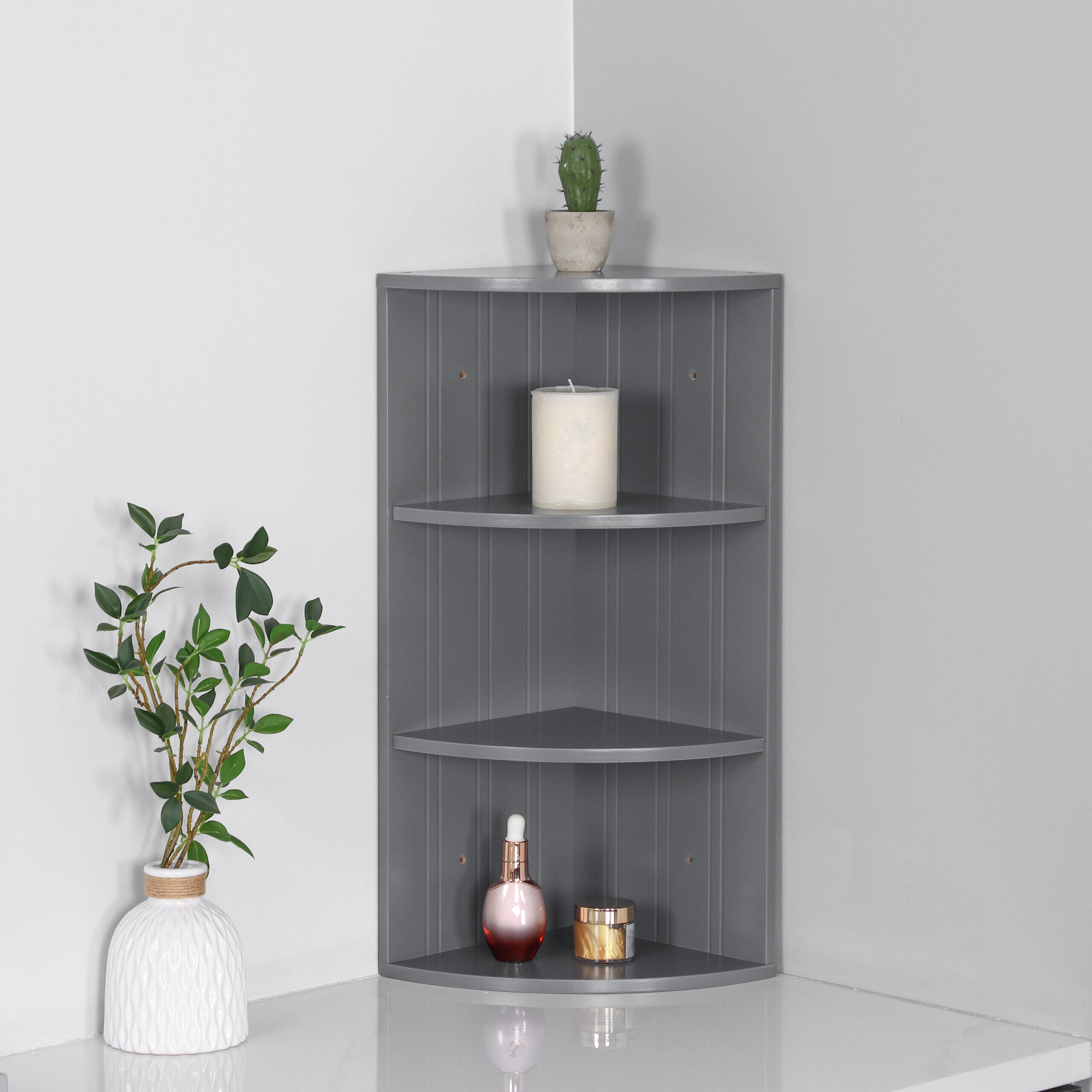 Ein graues Eckregal an einer weißen Wand mit Kerze und Kosmetik, daneben eine Pflanze in Vase.
