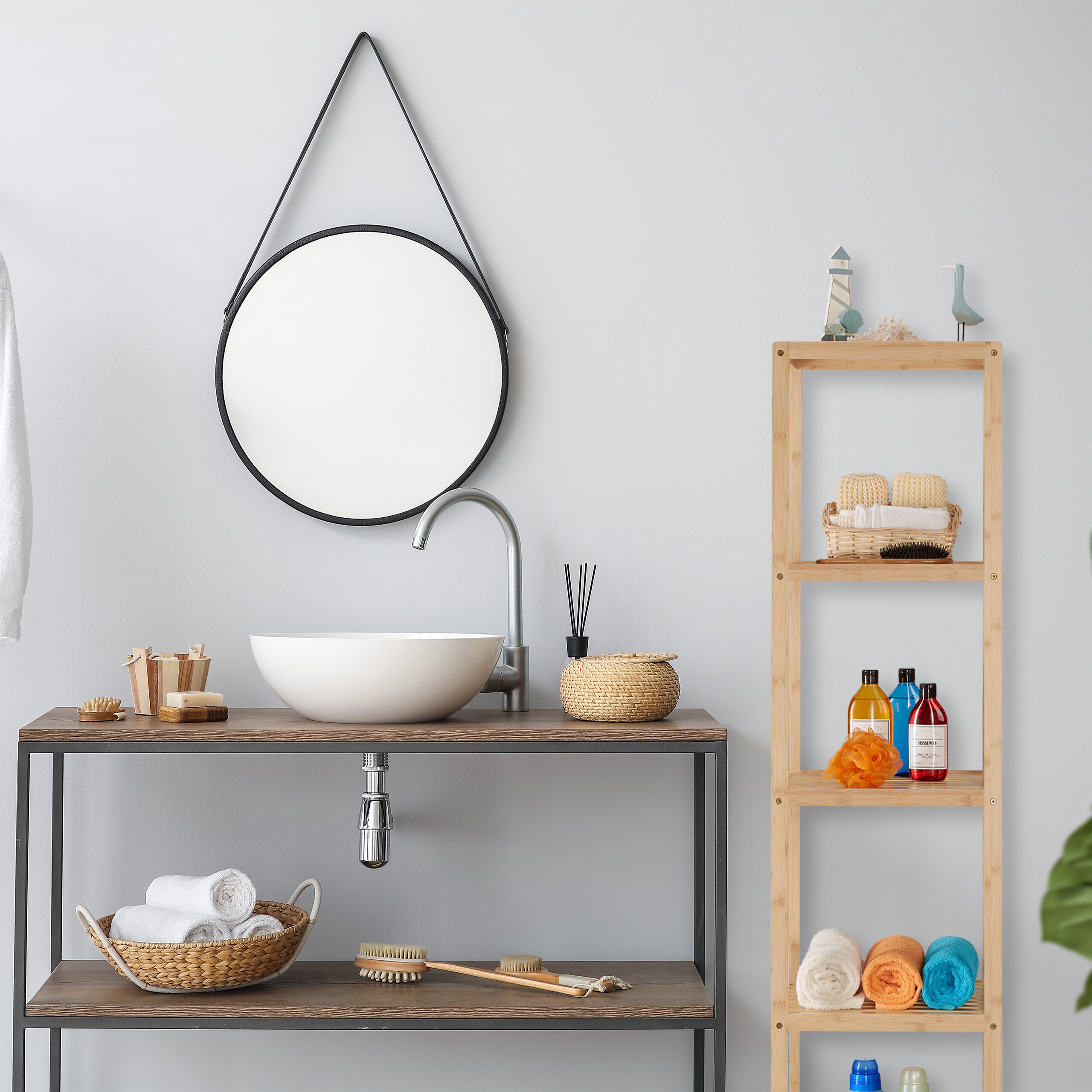 Badezimmer mit Waschbecken auf Holztisch, rundem Spiegel an grauer Wand und Holzregal voller Badutensilien.