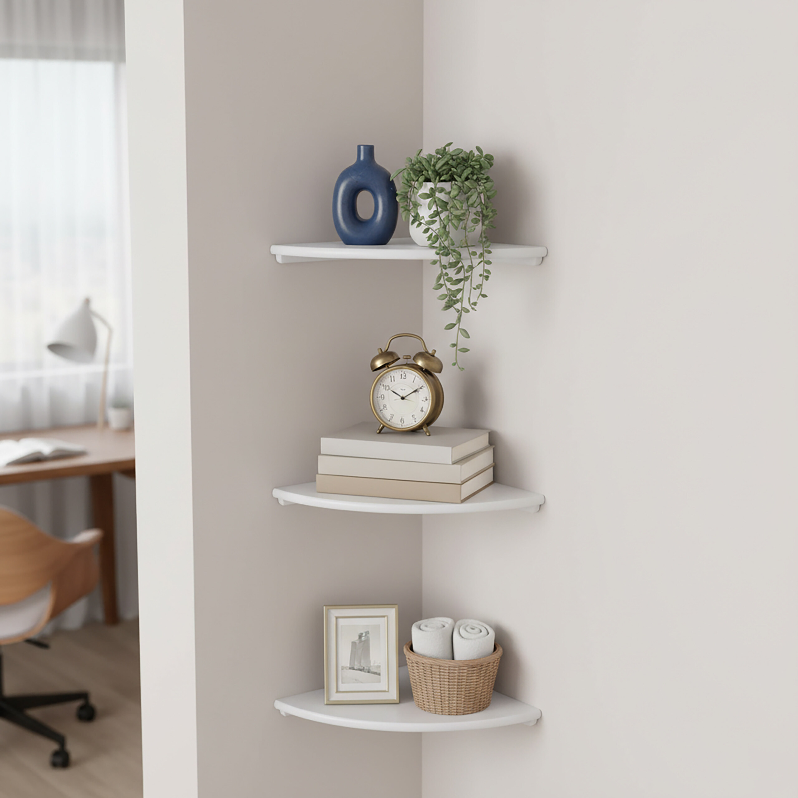 Drei weiße Eckregale mit Dekoration an einer hellen Wand, im Hintergrund ein Schreibtisch.