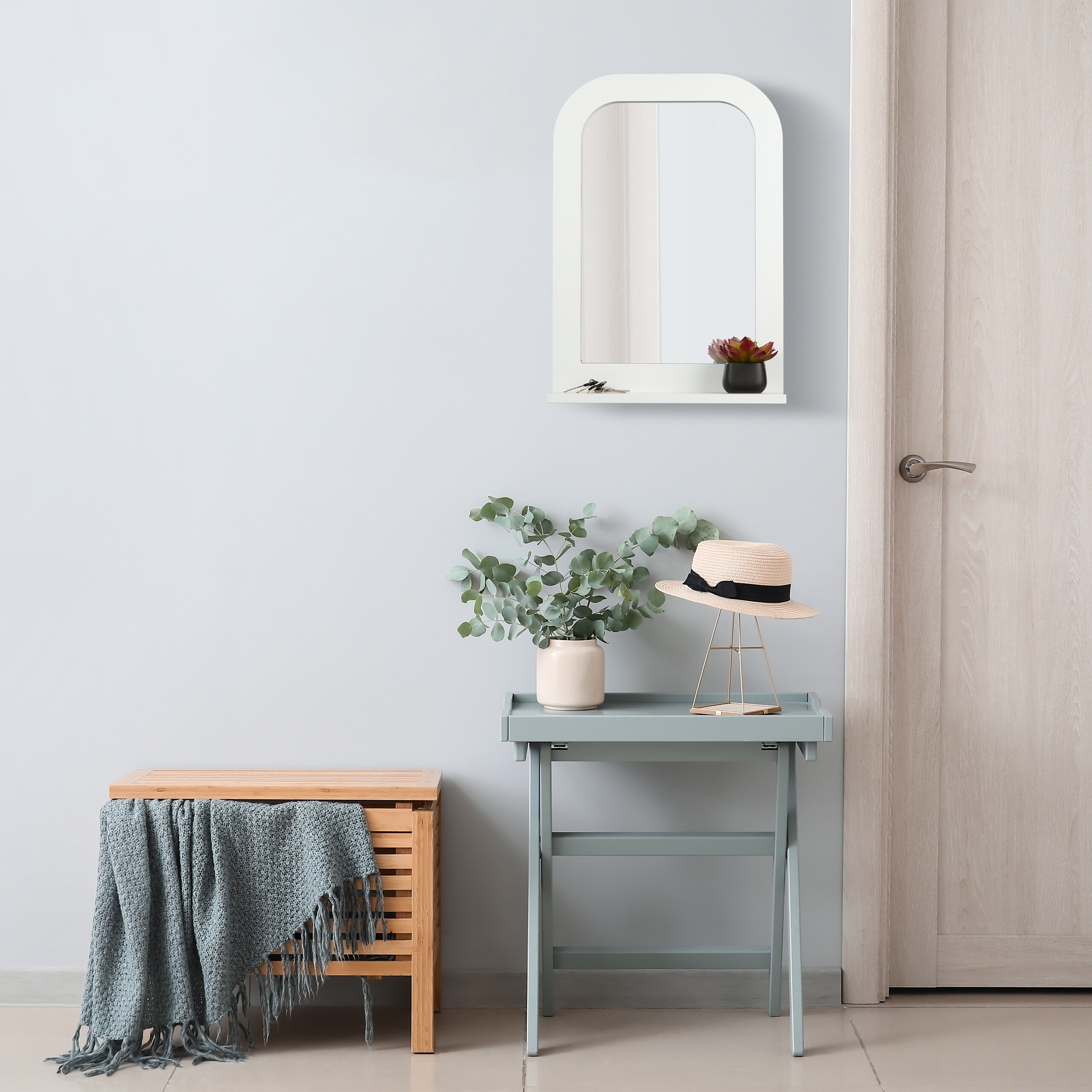 Ein heller Eingangsbereich mit Holztruhe, blauer Bank, Eukalyptuszweigen, Hut und weißem Spiegel an der Wand.