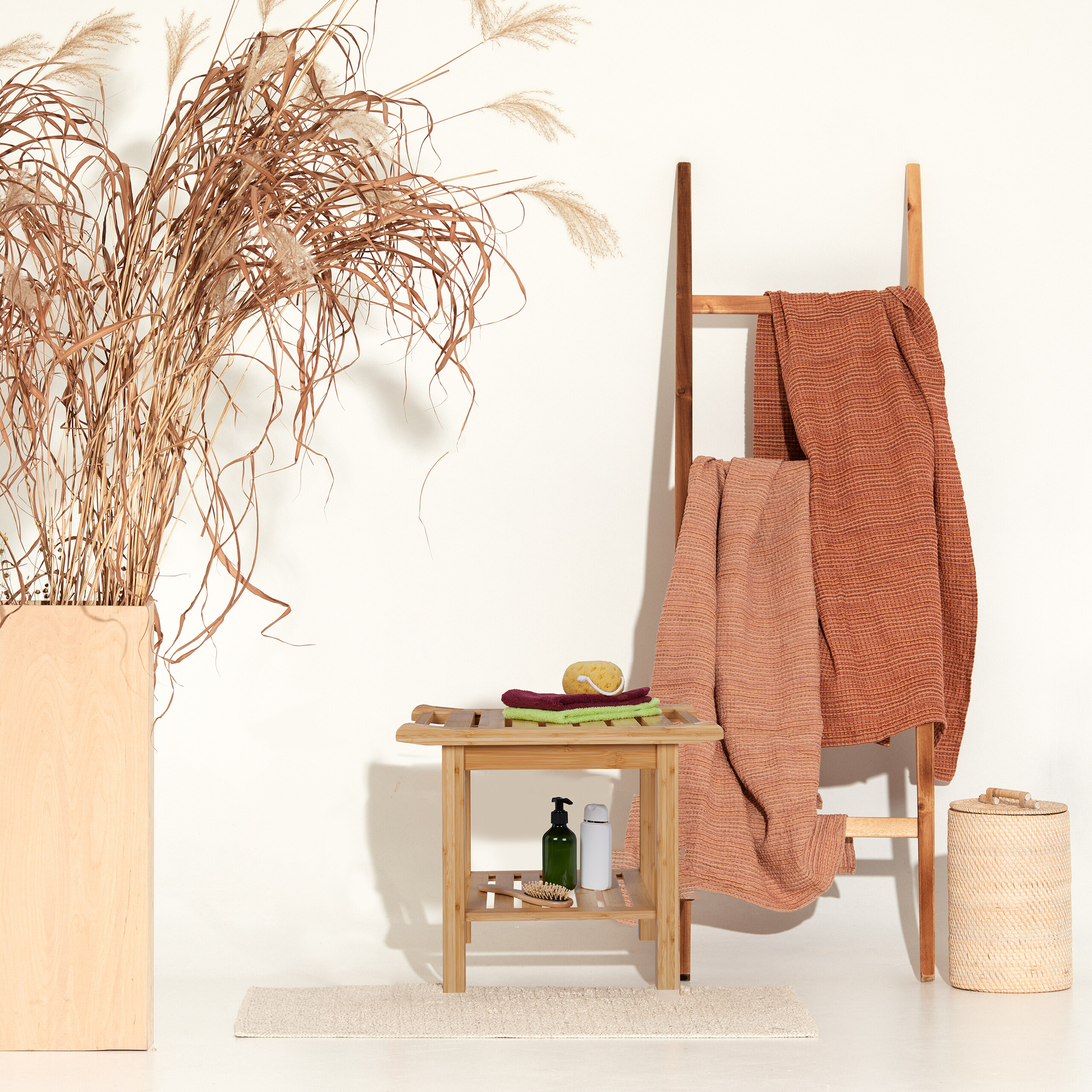 Badezimmerdekor mit Bambusbank, Holzleiter, Handtüchern, großen Trockengräsern in einer Vase und einem geflochtenen Korb.