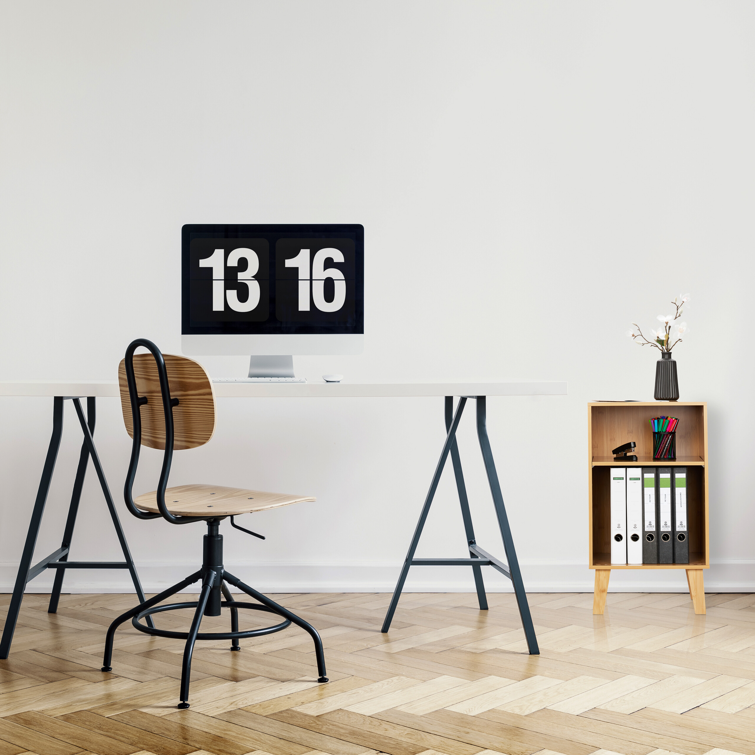 Ein weißer Schreibtisch mit Computer und Stuhl auf Holzboden vor weißer Wand.
