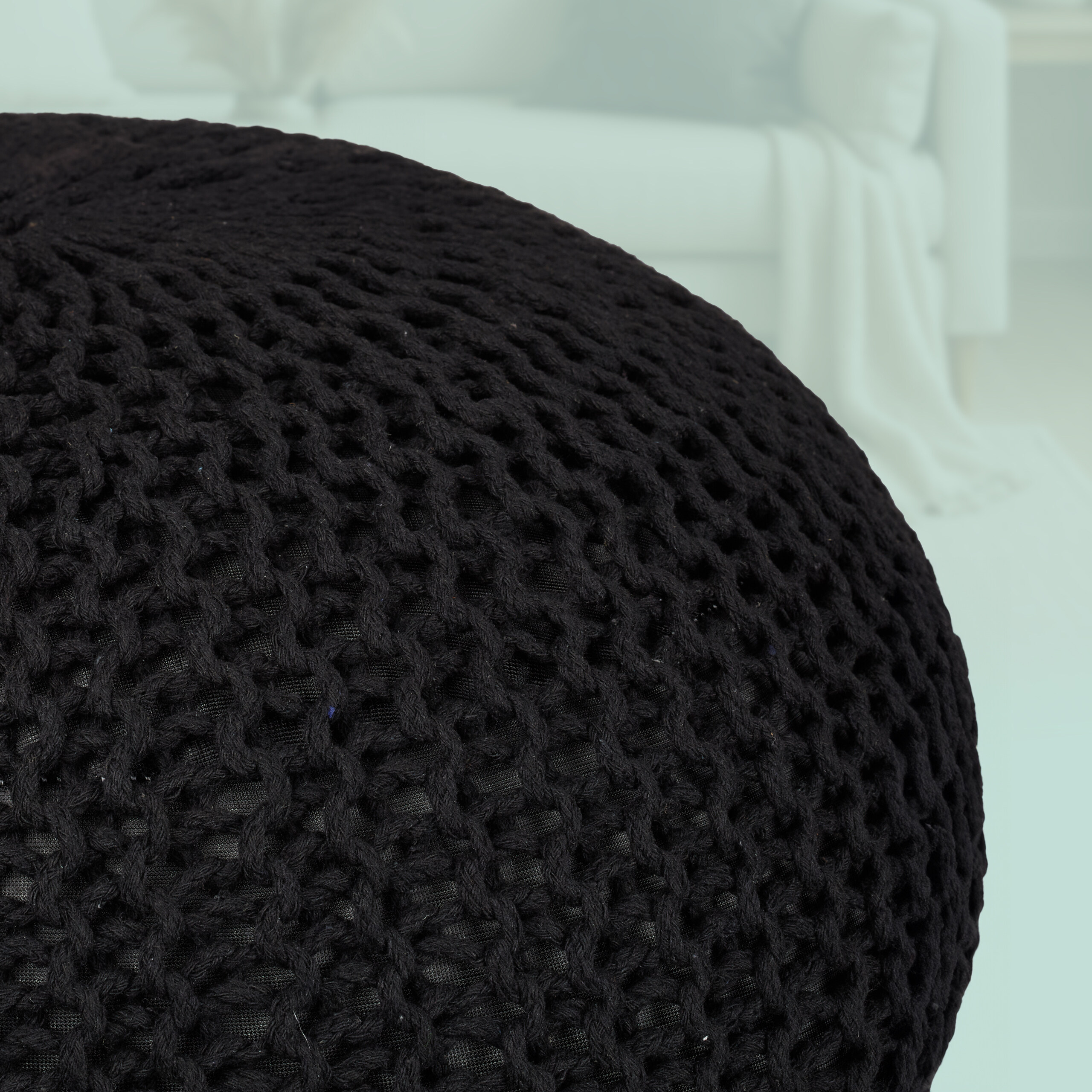 Ein schwarzer Strickpouf im Vordergrund vor einem verschwommenen hellen Zimmer.