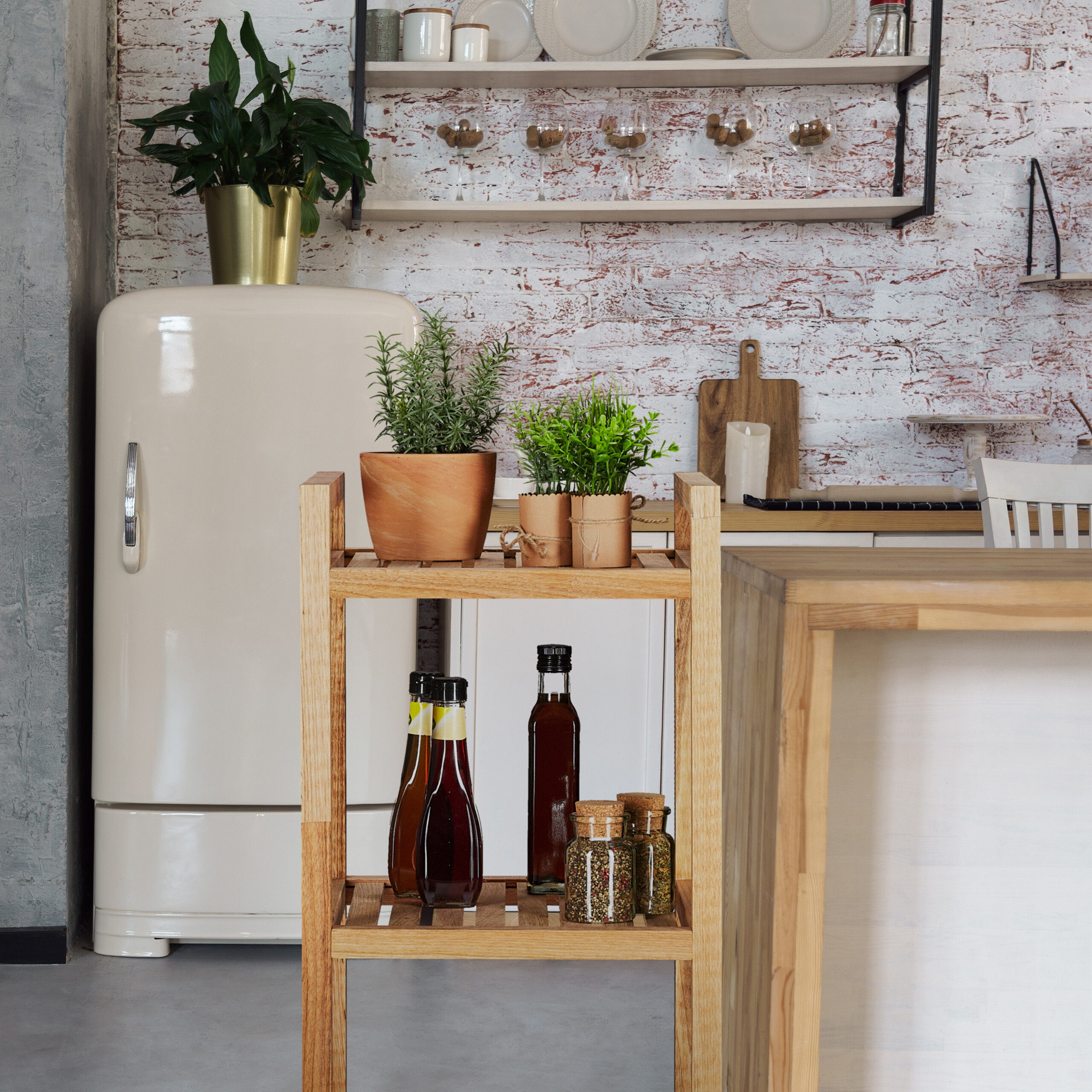 Eine rustikale Küche mit einem Retro-Creme-Kühlschrank, Ziegelwand und einem Holzregal mit Pflanzen und Flaschen.