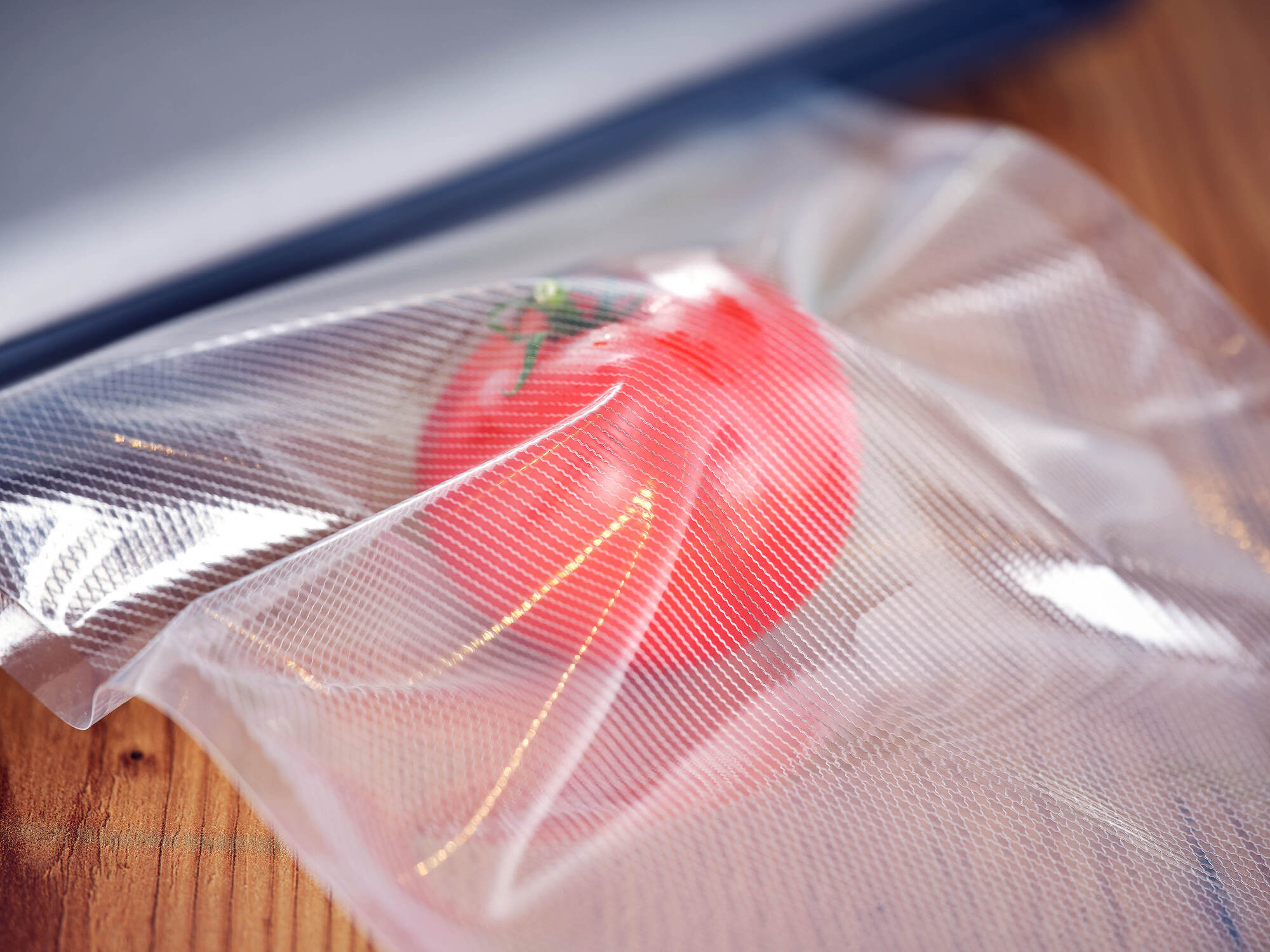 Un tomate rojo fresco dentro de una bolsa de vacío texturizada en una superficie de madera.
