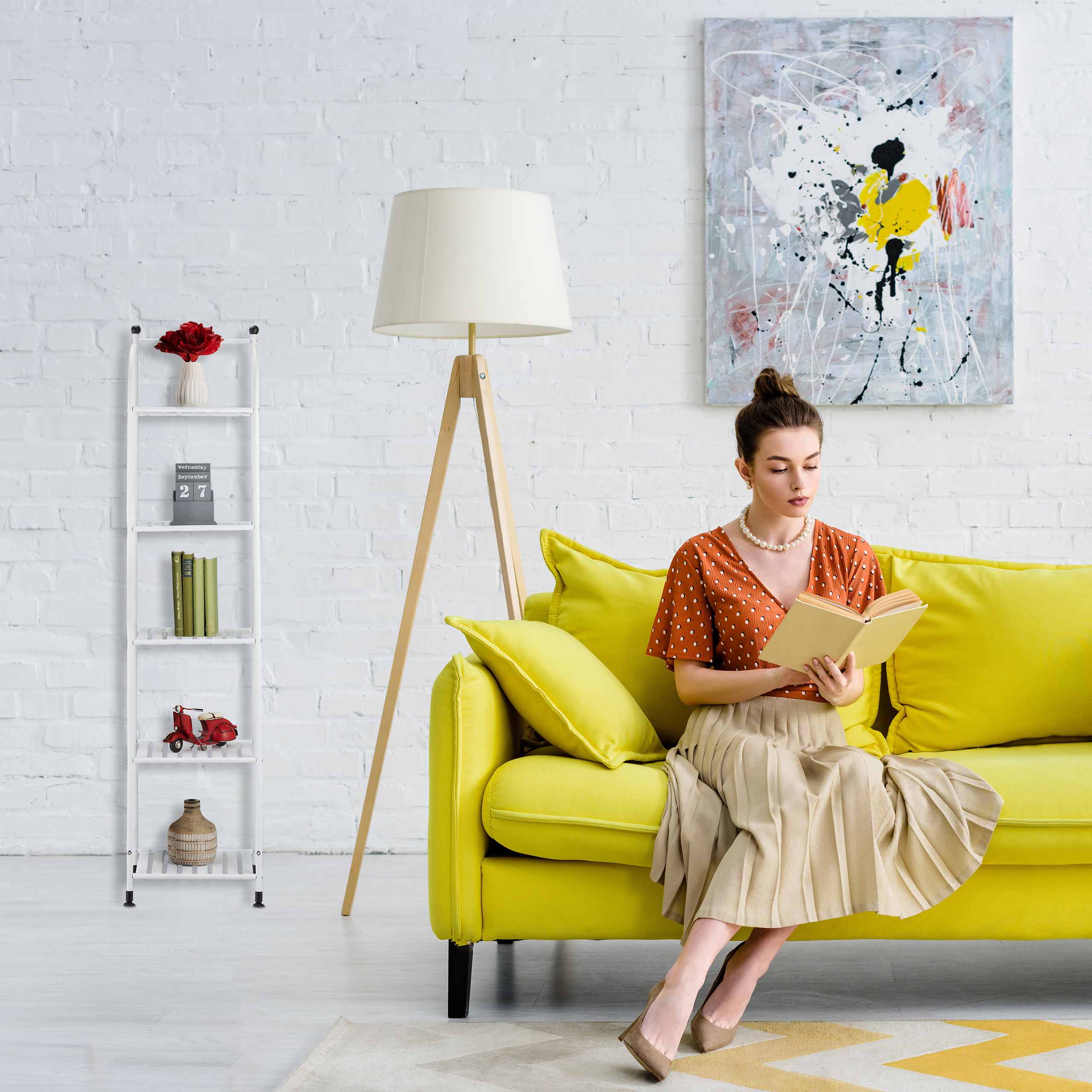 Eine Frau liest ein Buch auf einem gelben Sofa in einem hellen Raum mit weißer Backsteinwand.