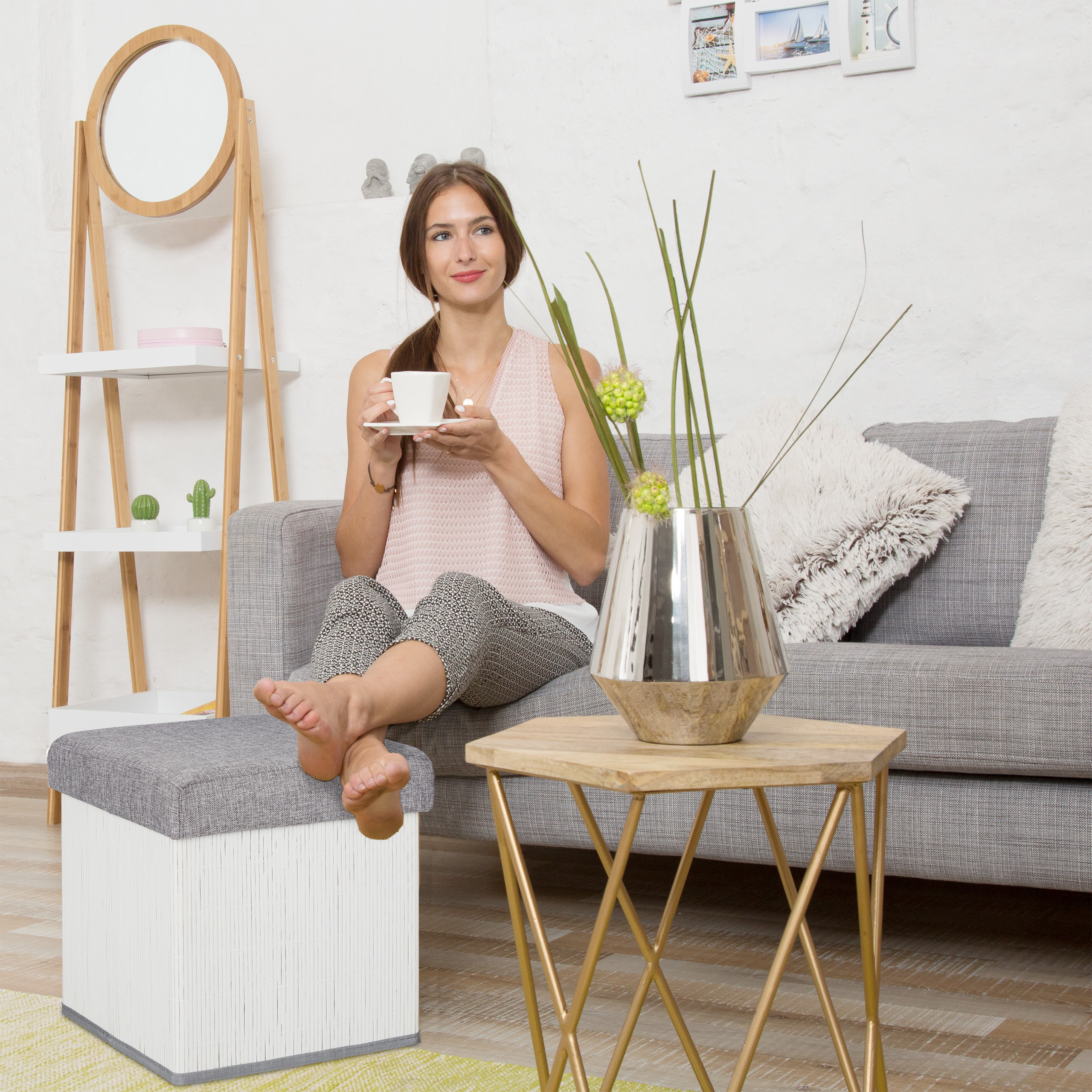 Eine lächelnde Frau mit Tasse entspannt auf einem Sofa, Füße auf einem Hocker, neben einem Holztisch.