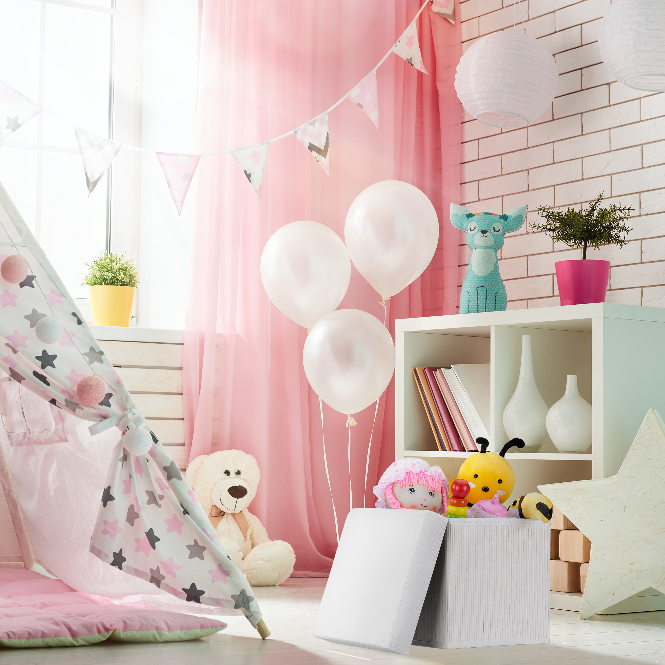 Kinderspielzimmer mit rosa Vorhängen, weißen Ballons, einem Tipi-Zelt, Kuscheltieren und einem Regal an einer Backsteinwand.