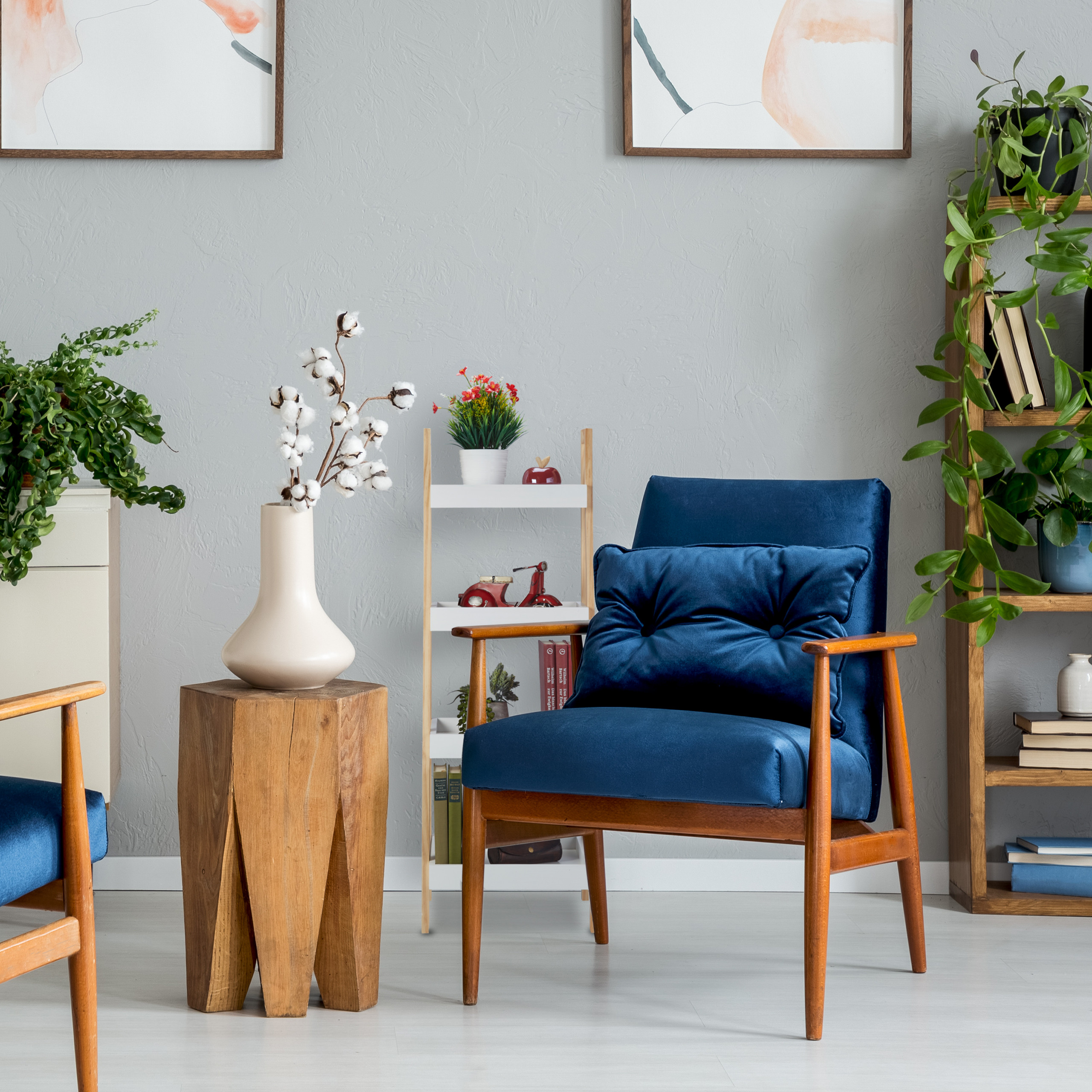 Gemütlicher grauer Raum mit blauem Sessel, Holztisch, Pflanzen, Bücherregal und abstrakten Bildern an der Wand.