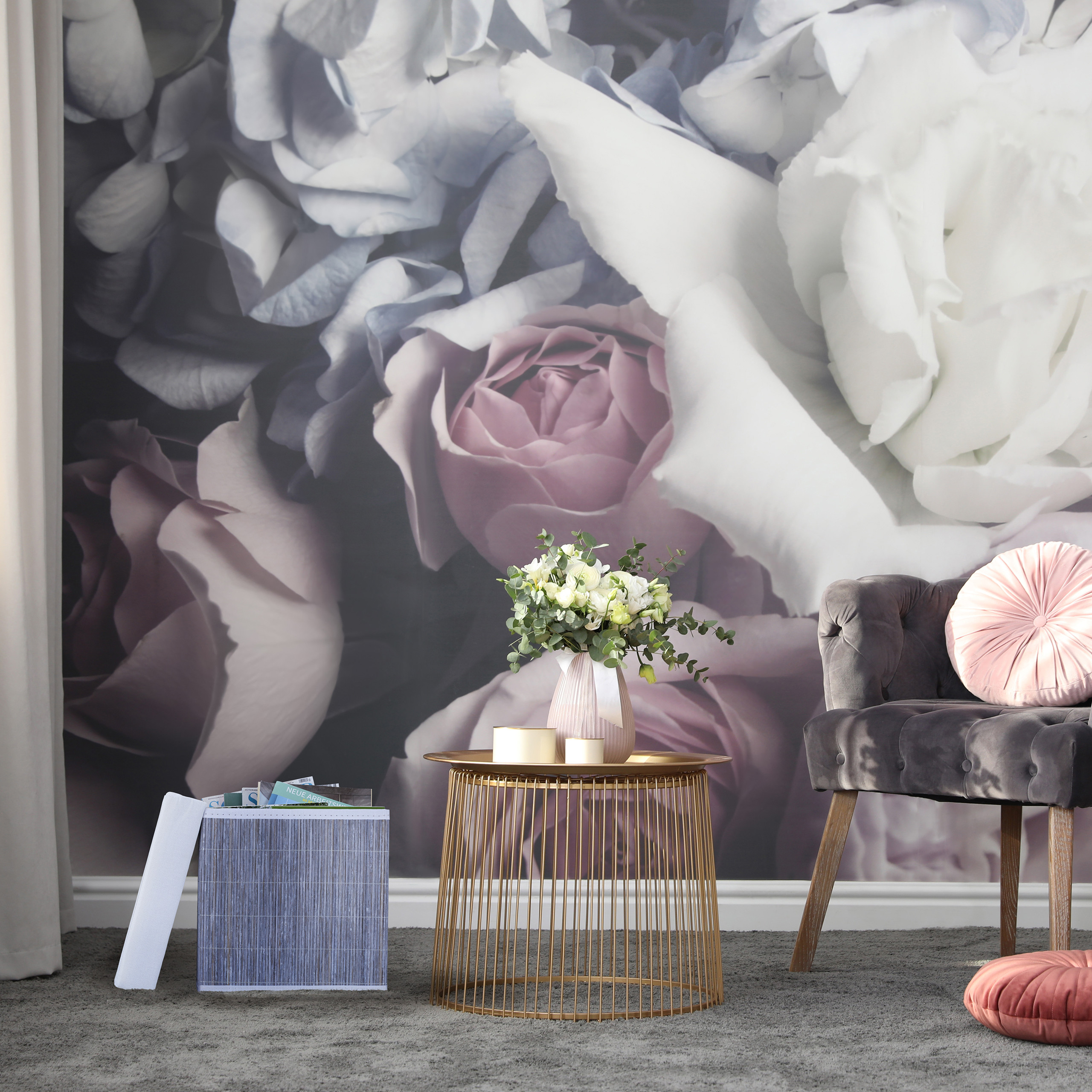 Ein stilvolles Wohnzimmer mit großem Blumenwandbild, goldenem Tisch, grauem Sessel und rosafarbenem Kissen.