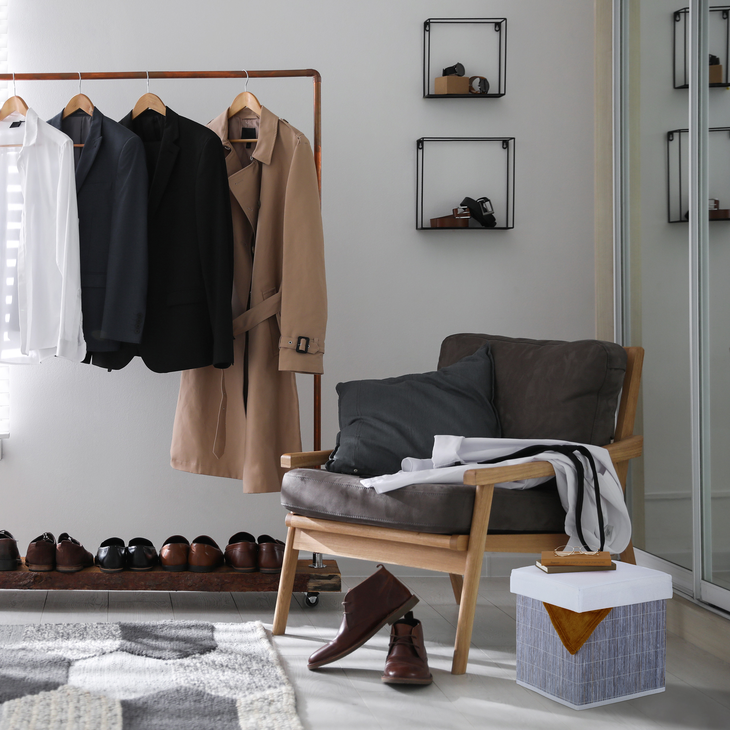 Kleiderständer mit Mänteln, Sesseln mit Kissen, Schuhen unten und Wandregalen im modernen Zimmer.