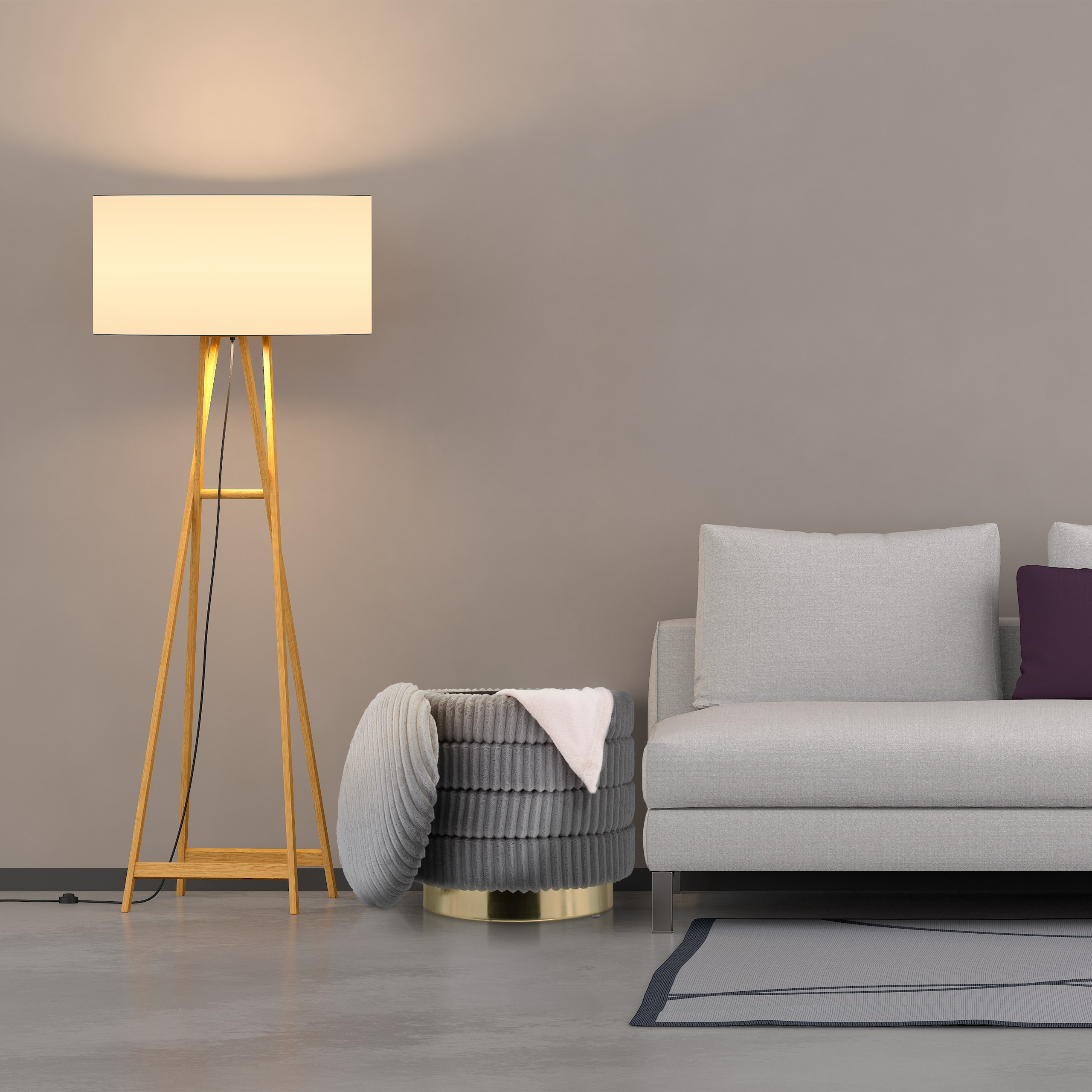 Eine beleuchtete Holz-Stehlampe, ein grauer Hocker mit Decke und ein graues Sofa mit violettem Kissen an einer Wand.
