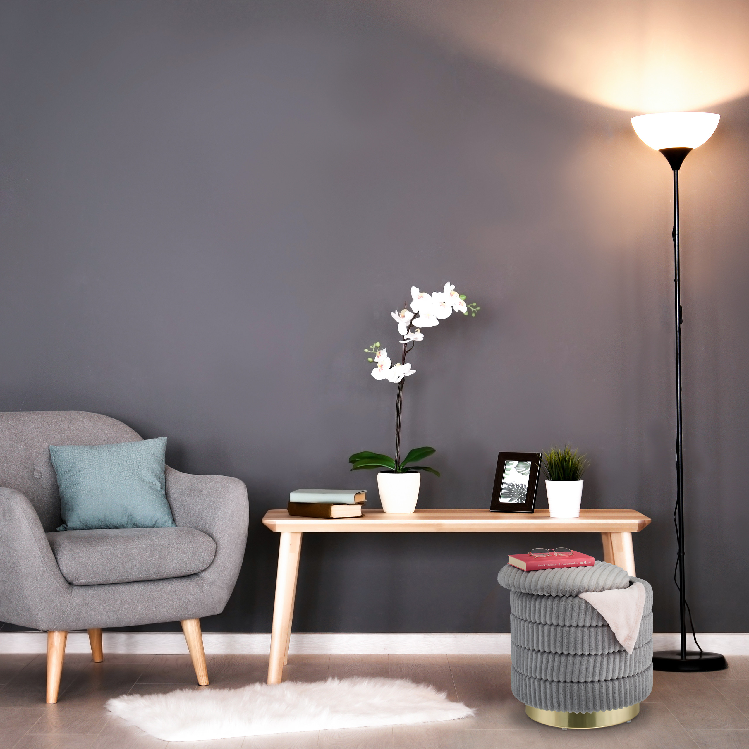 Grauer Sessel, Holztisch mit Orchidee und Lampe vor dunkler Wand.