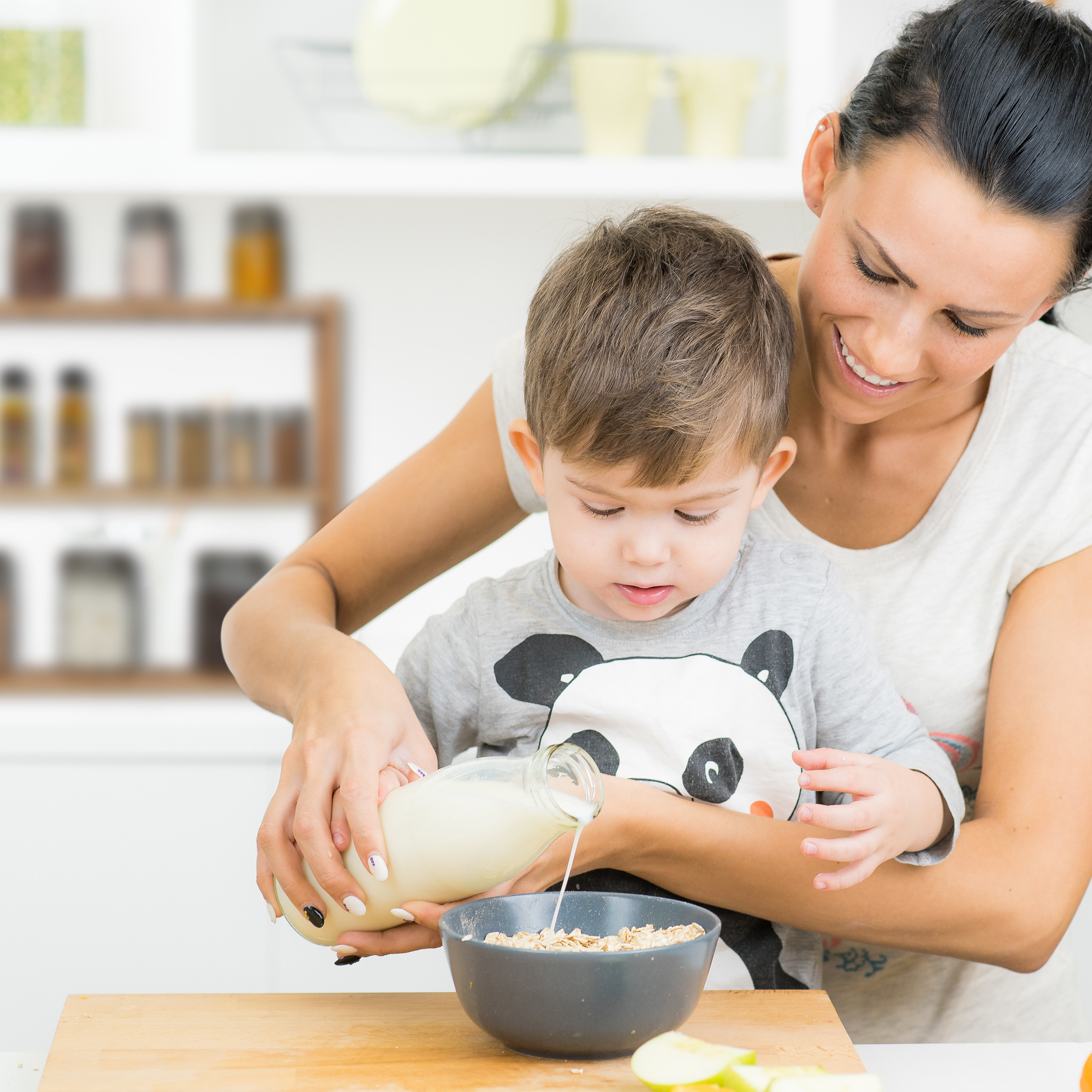 Eine Frau gießt Milch in eine Müslischüssel für einen kleinen Jungen in einer Küche.