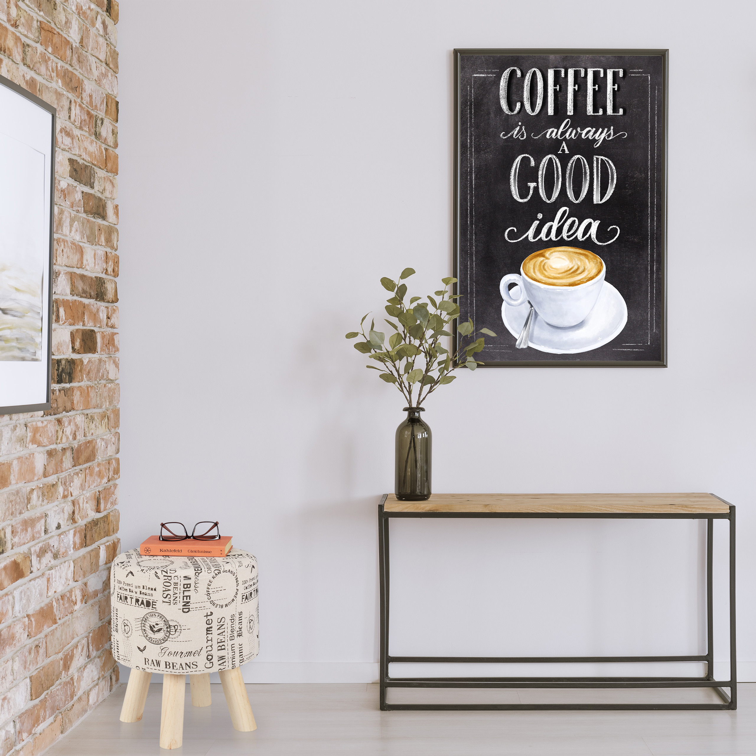 Ein Kaffeebild hängt über einem Tisch mit Pflanze, neben einer Ziegelwand und einem bedruckten Hocker.