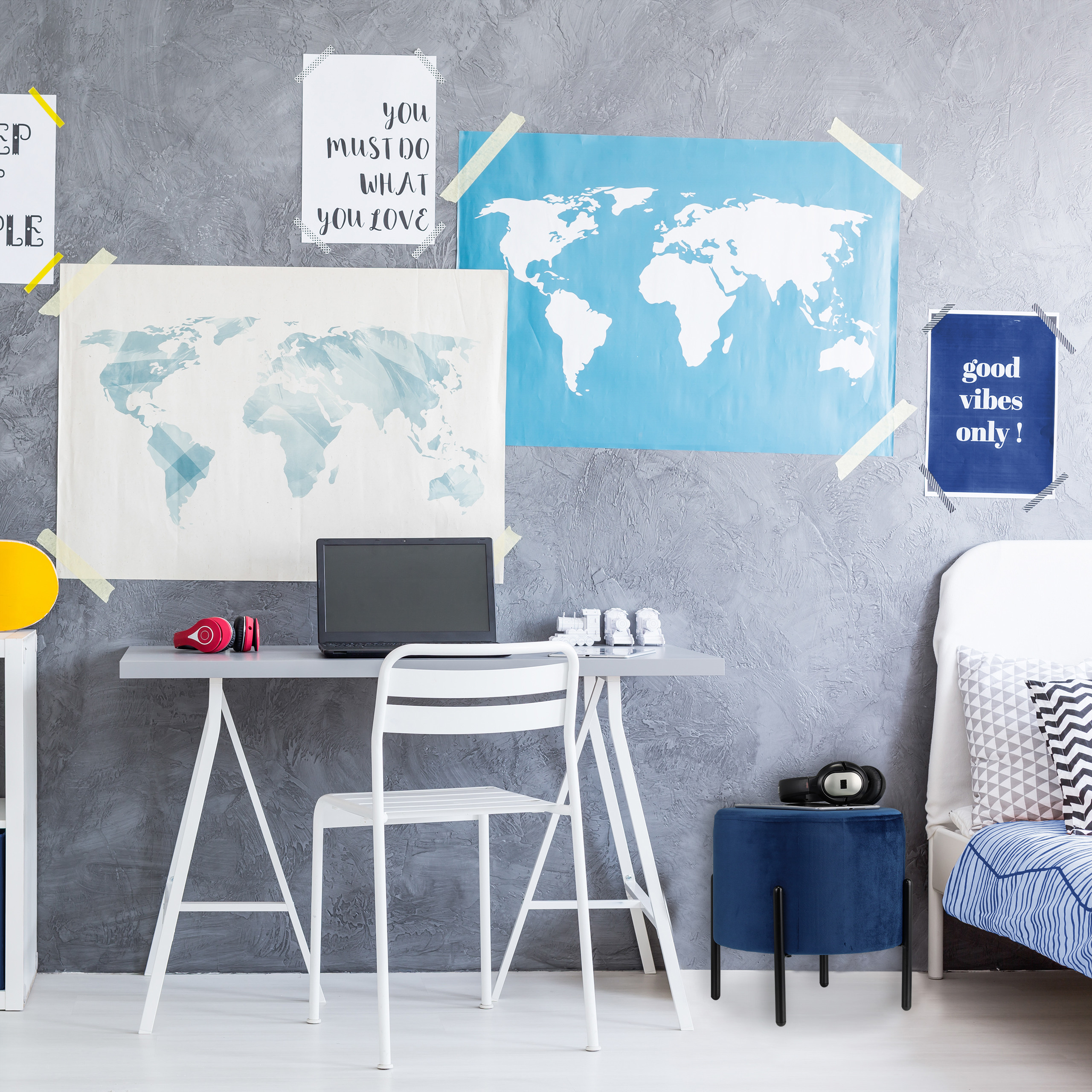 Ein Teenagerzimmer mit grauem Betonwand, Schreibtisch, Laptop, Weltkarte und weißem Stuhl.