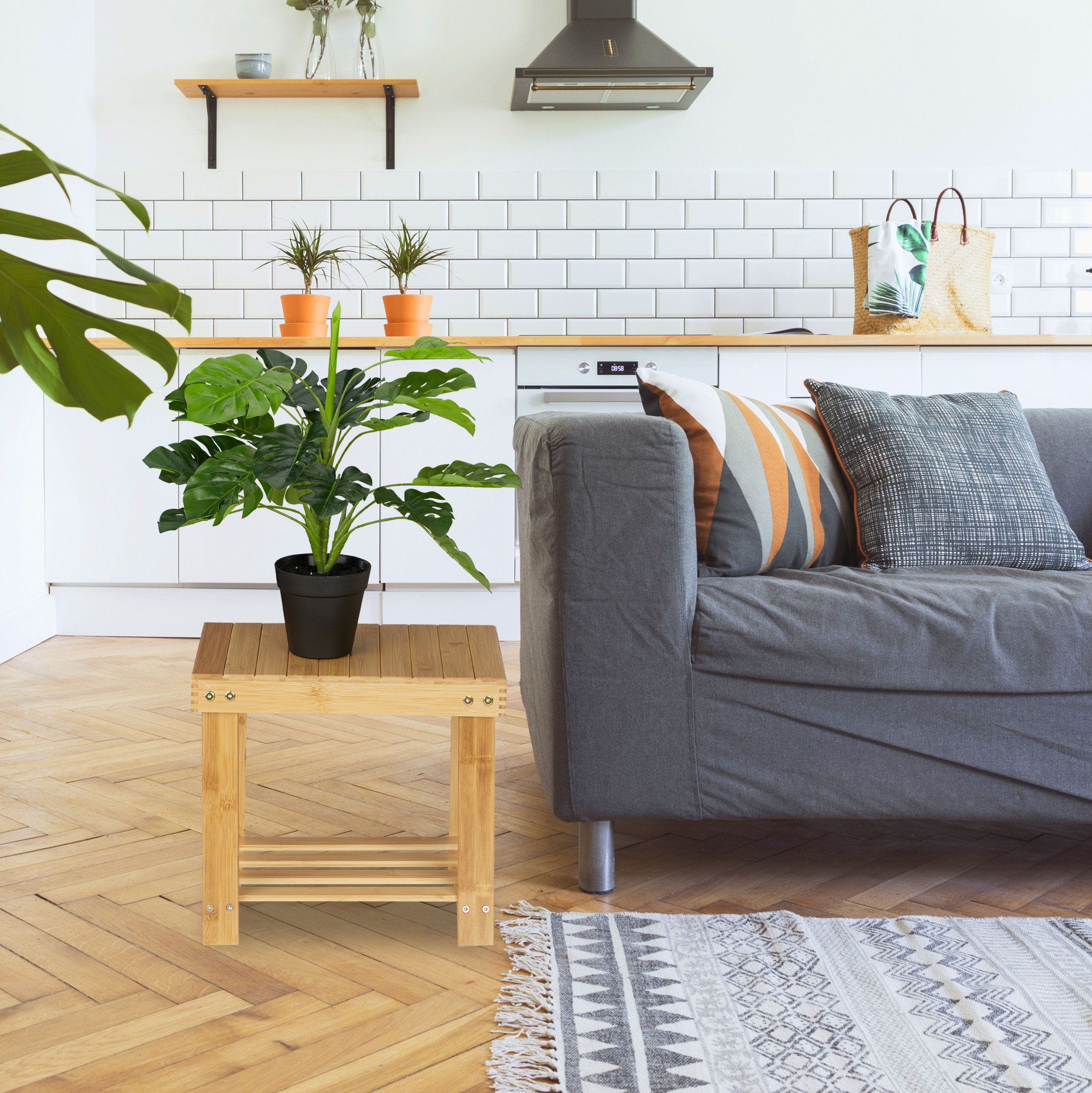 Wohnzimmer mit grauem Sofa, Holztisch, Topfpflanze und einer weißen Küche im Hintergrund.