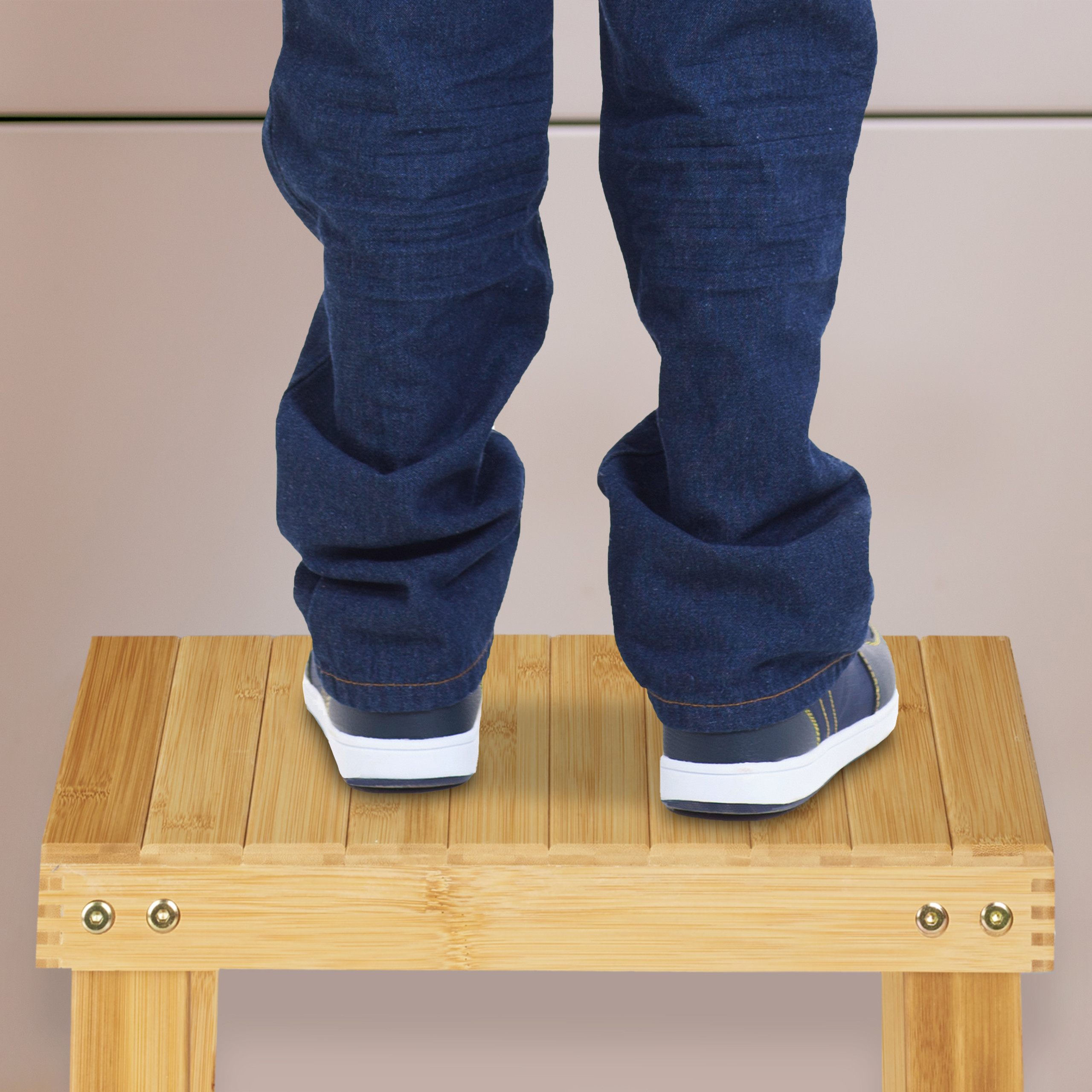Person in blauen Jeans und Turnschuhen steht auf einem kleinen Holzhocker vor einer Wand.