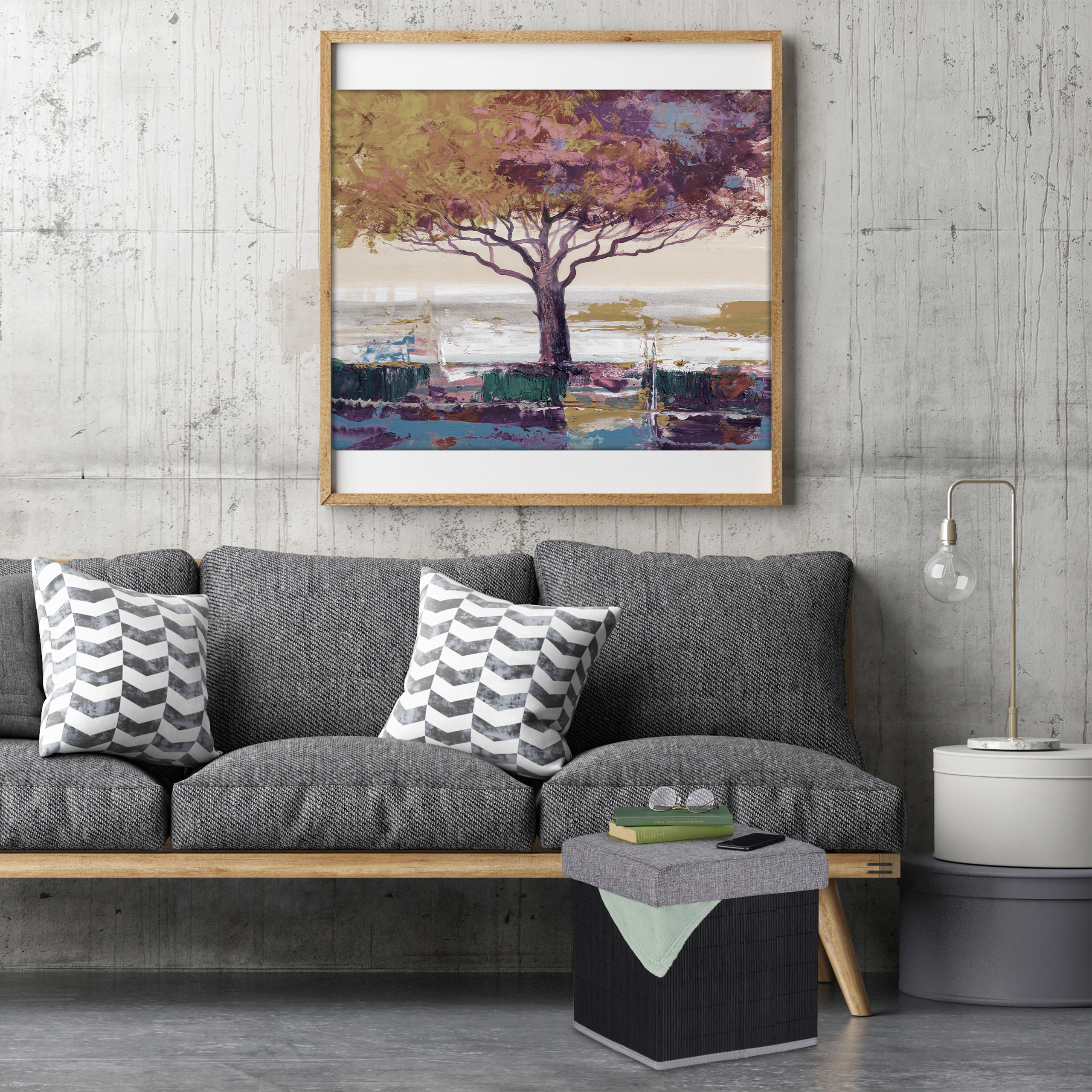 Ein graues Sofa mit Kissen steht an einer Betonwand unter einem gerahmten abstrakten Baumgemälde und neben einer Lampe.