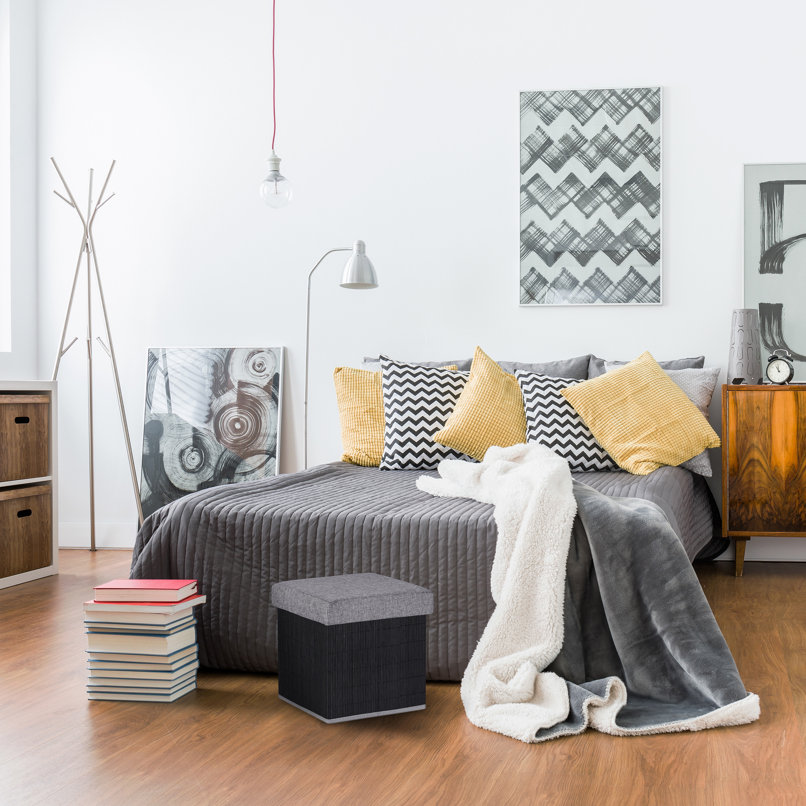 Gemütliches Schlafzimmer mit grauem Bett, gelben Kissen, einer Holzkommode und Kunstwerken an der Wand.