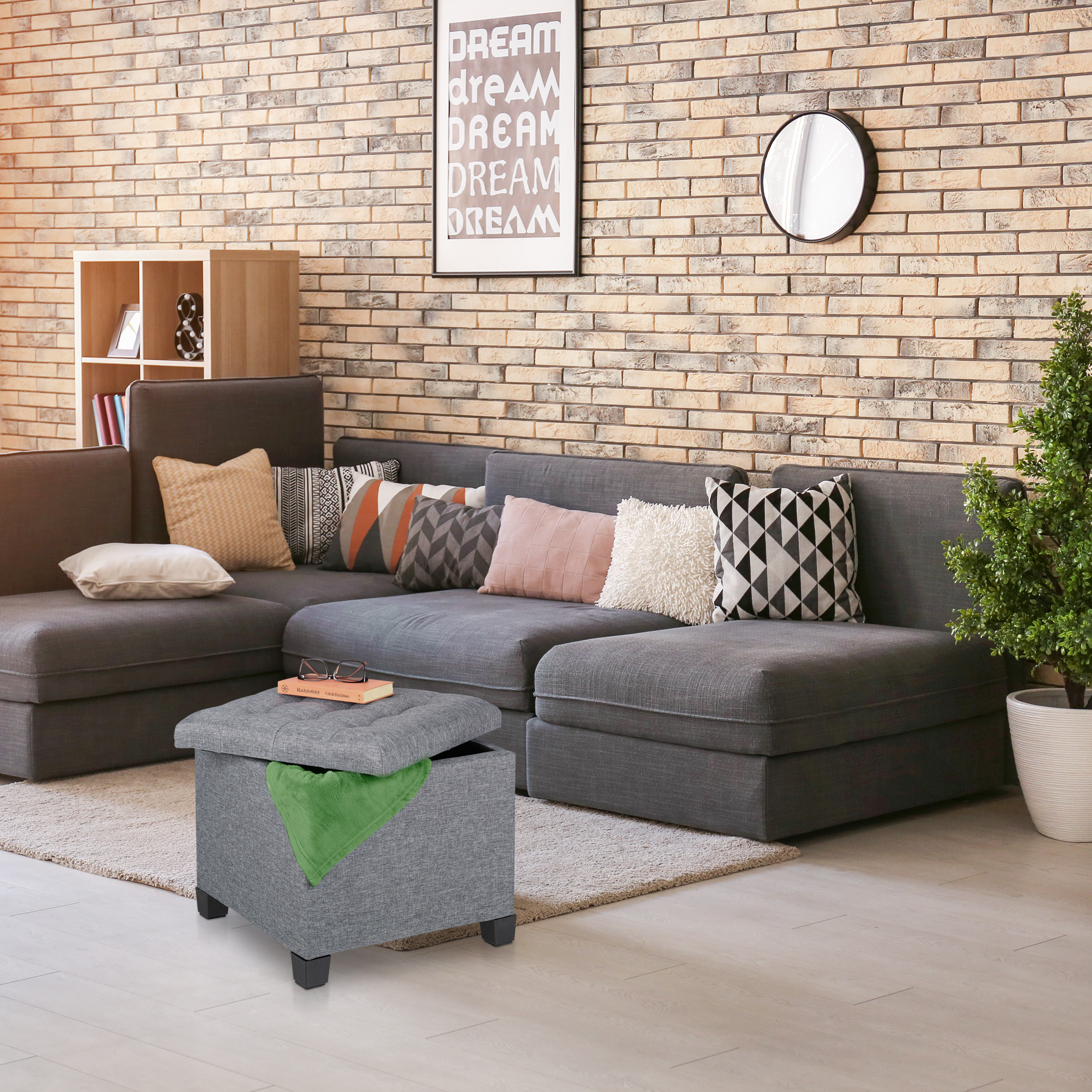 Gemütliches Wohnzimmer mit grauem Sofa, Kissen, Hocker und Backsteinwand.