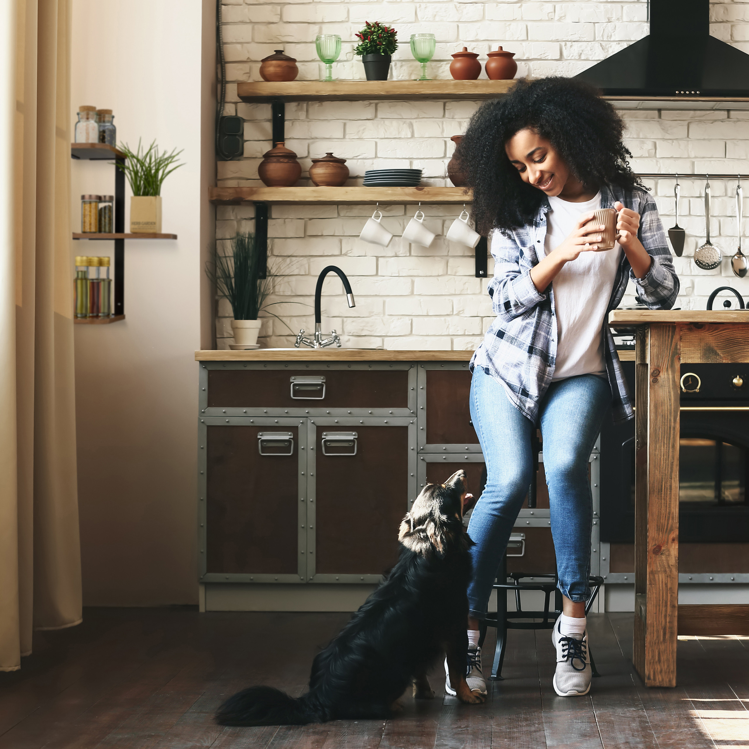 Eine Frau in einer Küche sitzt mit einer Tasse Kaffee, während ein Hund sie anschaut.