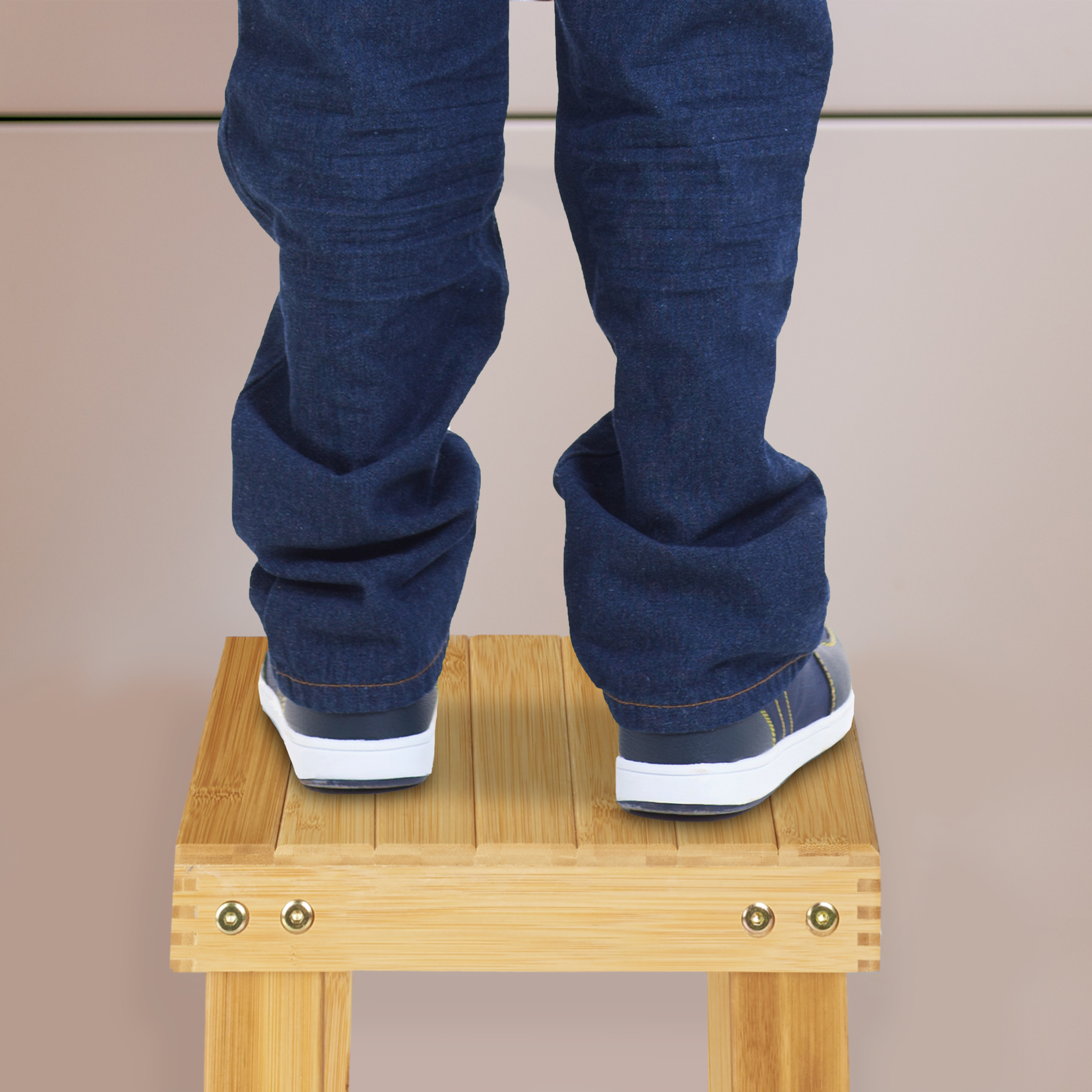 Person in blauen Jeans und Sneakers steht auf einem Holzhocker.