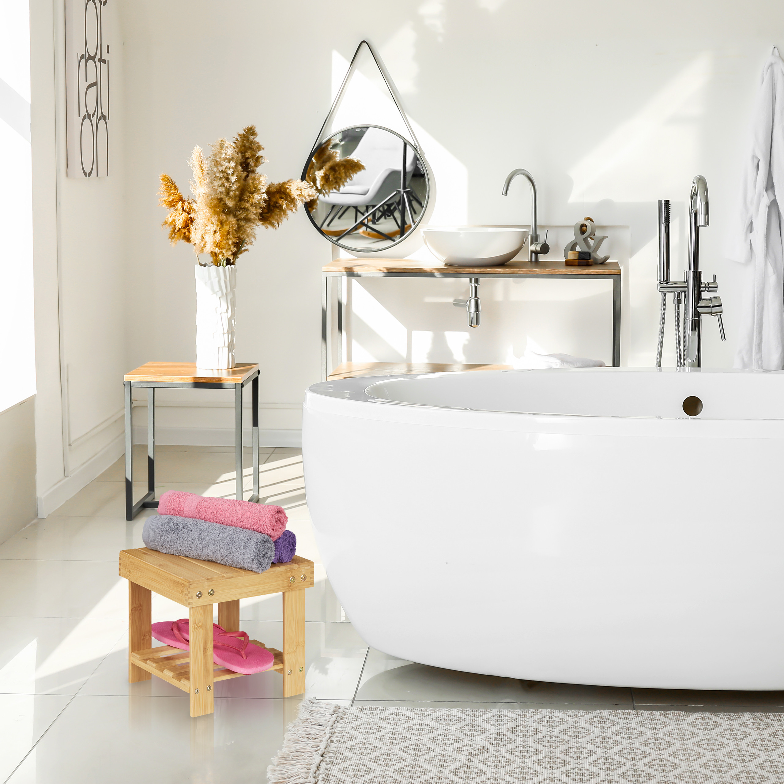 Moderne weiße Badewanne mit Handtüchern auf einem Holzschemel, Waschbecken und Spiegel in einem hellen Raum.