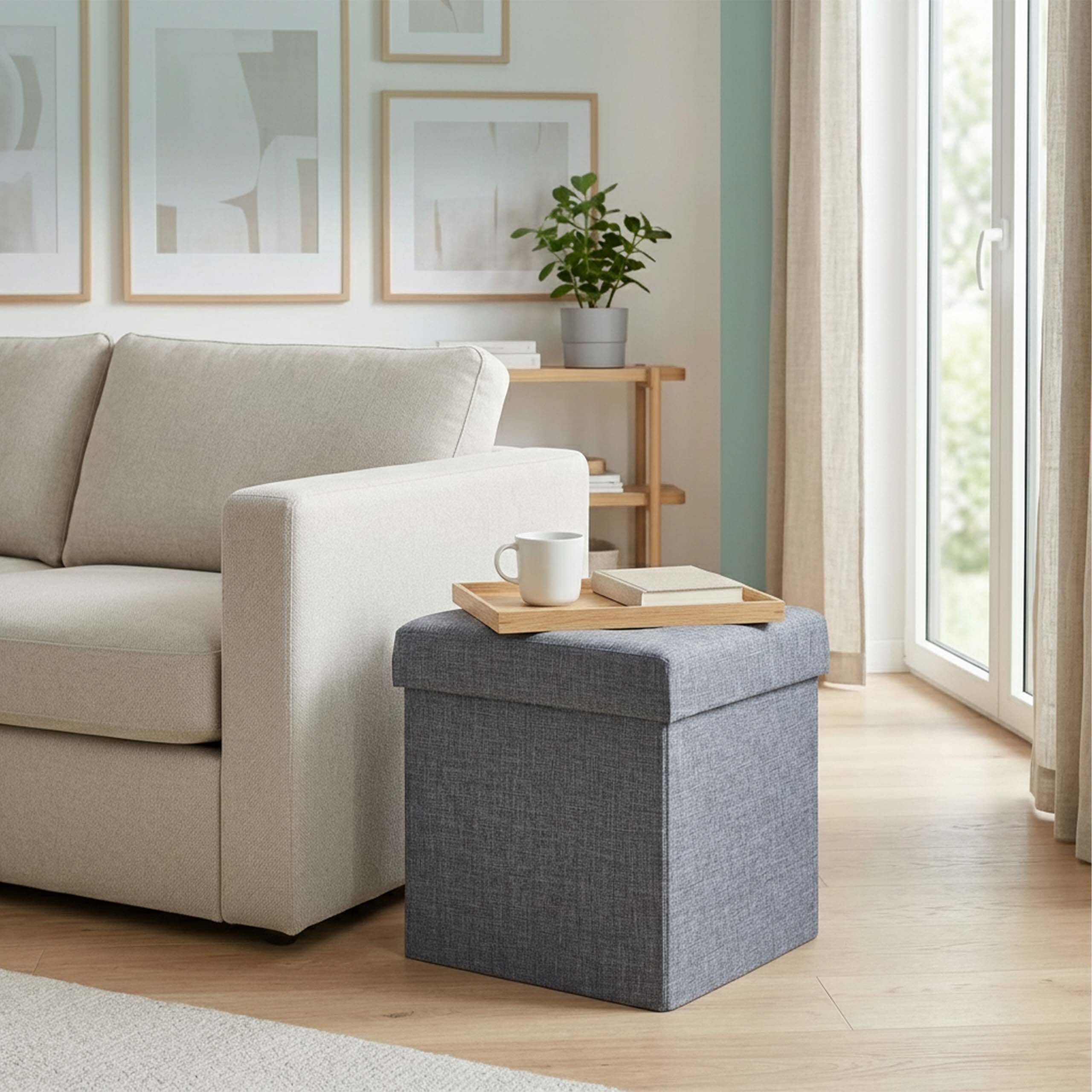 Beige Couch neben grauem Hocker mit Holztablett, Tasse und Buch in hellem Wohnzimmer.