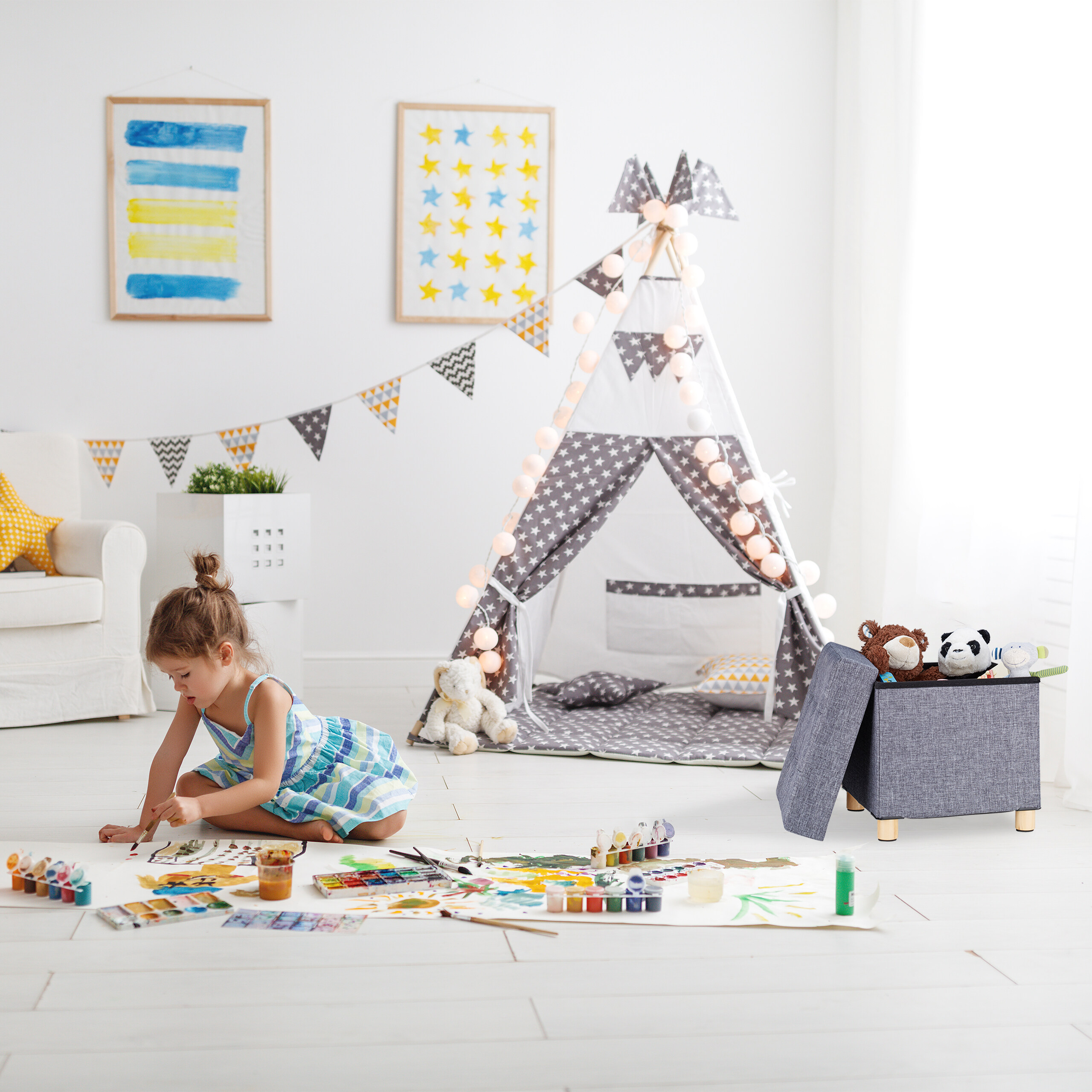 Ein kleines Mädchen sitzt auf dem Boden in einem hellen Kinderzimmer und malt auf großem Papier mit Wasserfarben.